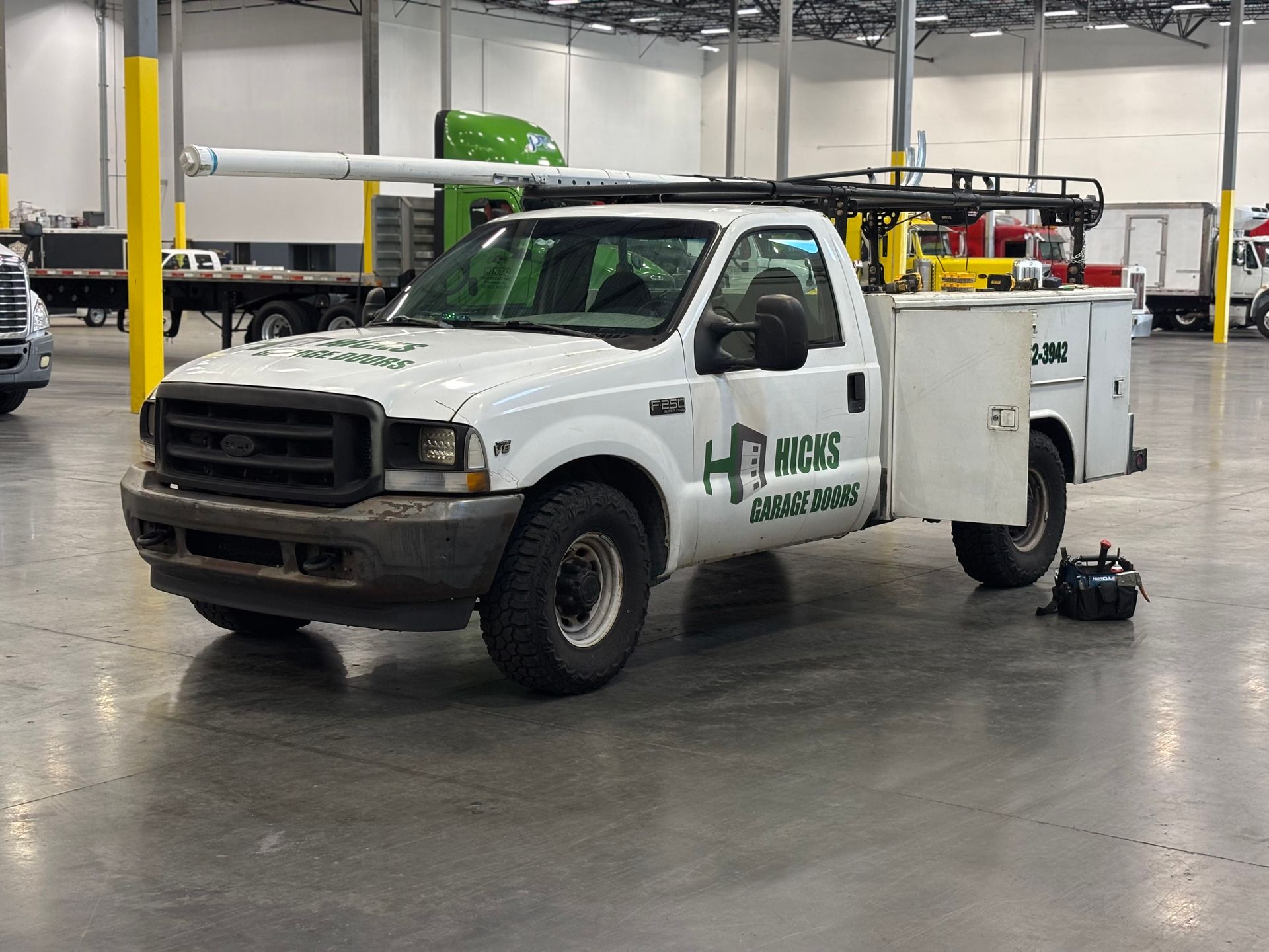 White utility truck with equipment in an indoor warehouse garage, parked on a polished floor.