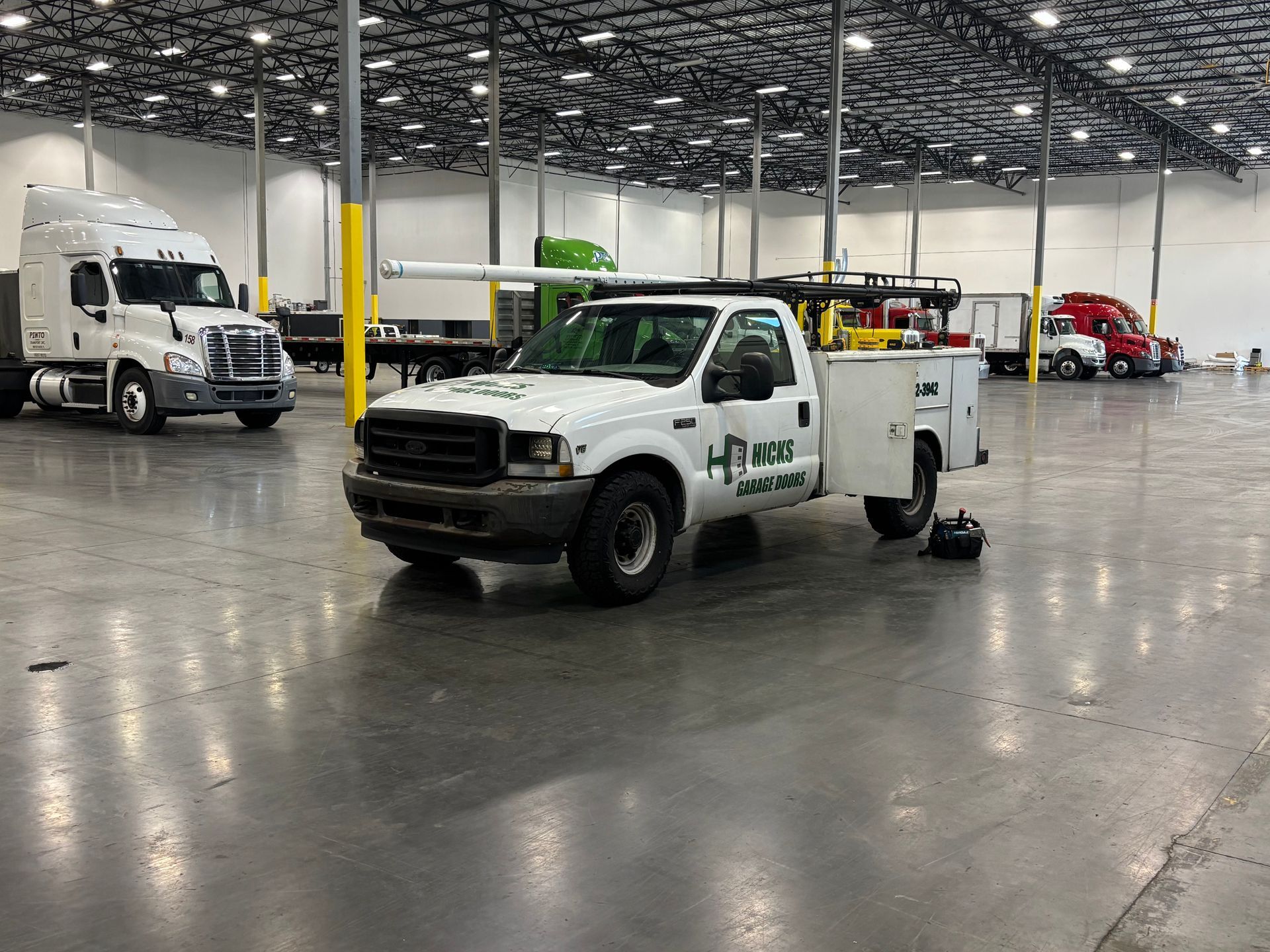 White utility truck in a large warehouse with another truck and a red forklift in the background.