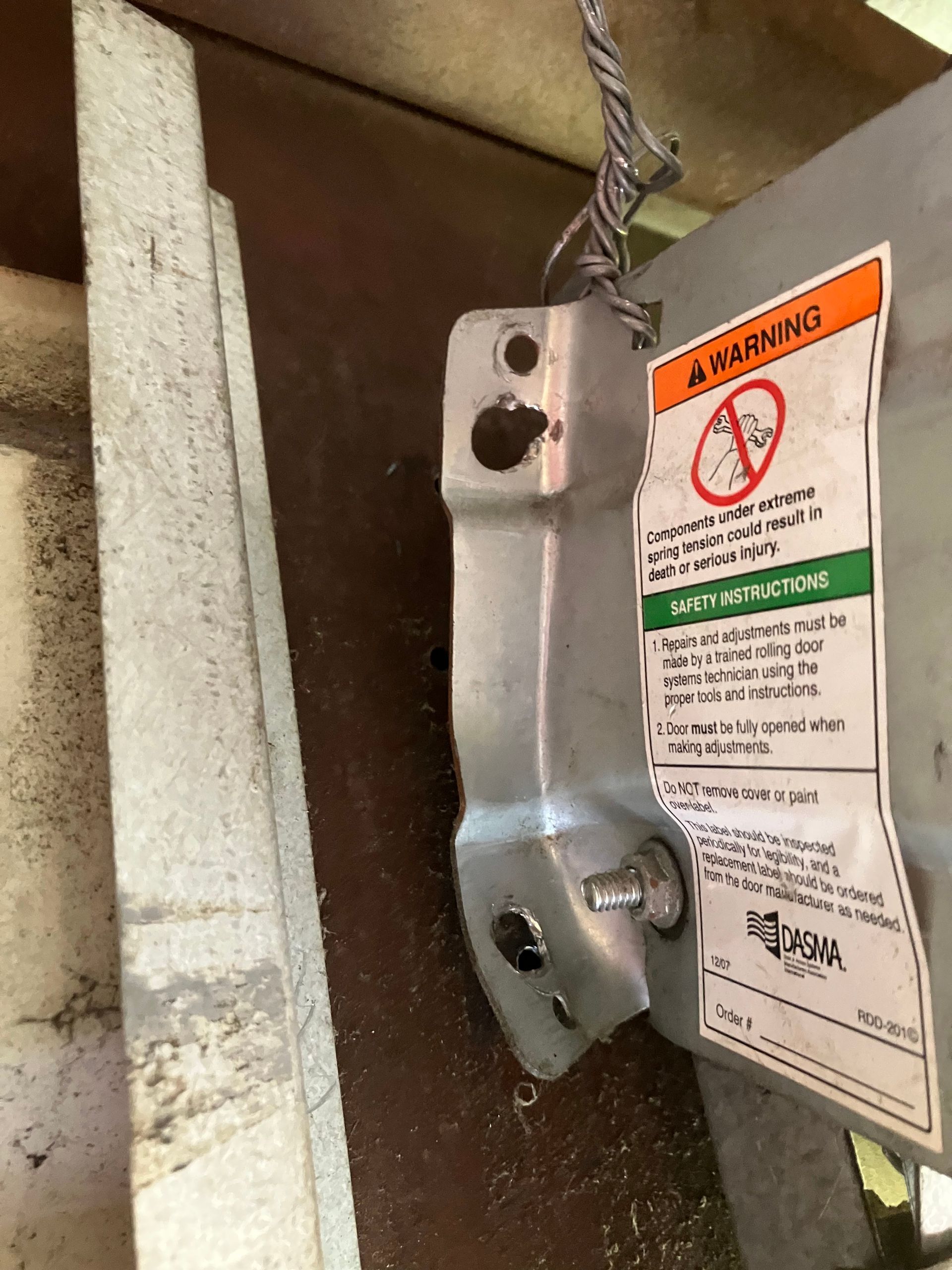 Close-up of a metal garage door opener bracket with warning label and hanging chain.