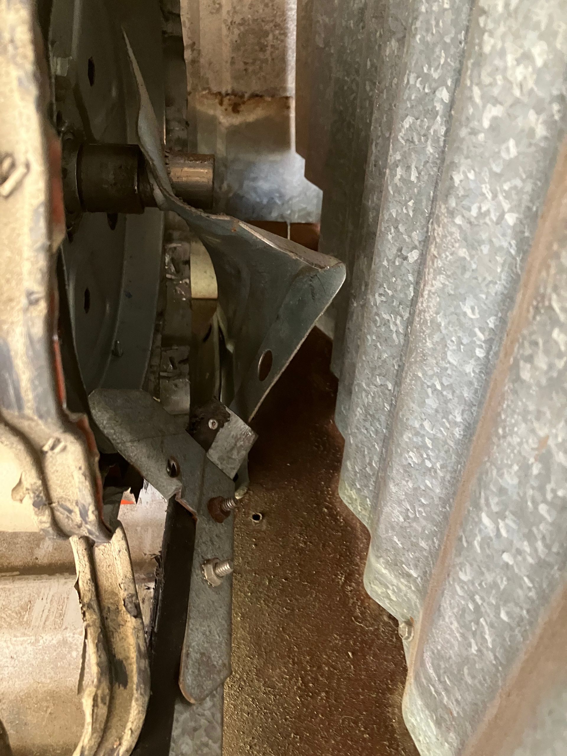 Close-up of a metal mechanical bracket beside corrugated metal, with dust and debris on the floor.