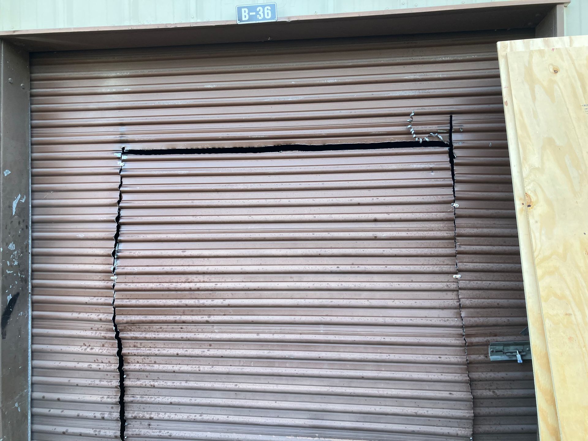 Closed brown metal roll-up door with a partially open top slat, framed by a concrete opening.