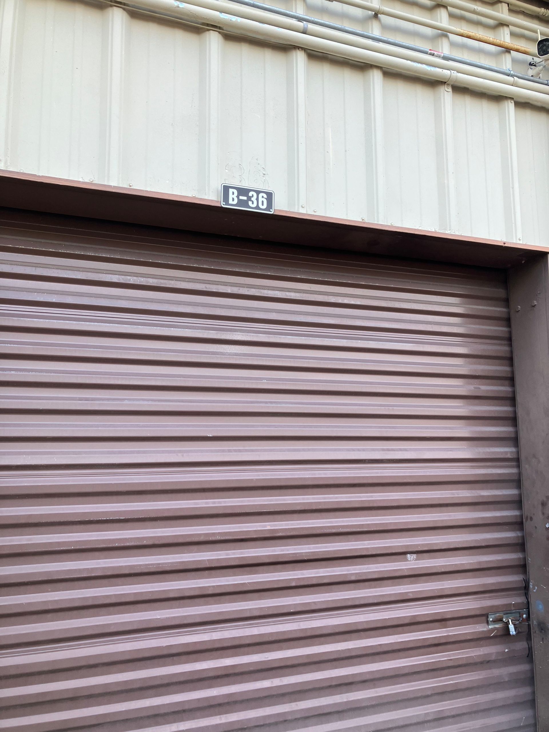 Closed brown roll-up metal door with a small number sign above it on a beige industrial building