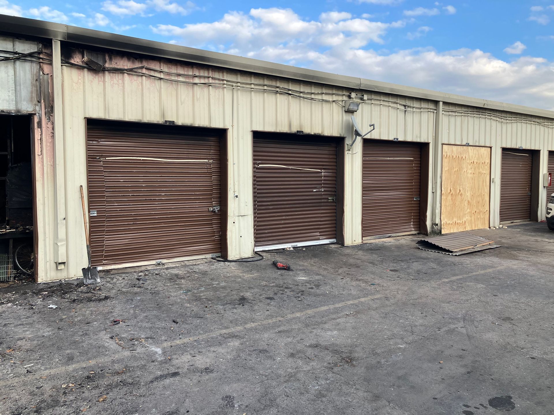Row of closed brown storage unit doors on a beige industrial building with gravel lot in front