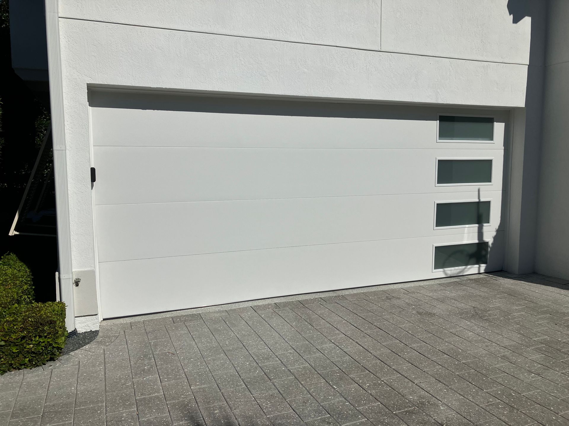 Modern white garage door with narrow glass panels beside a paved driveway