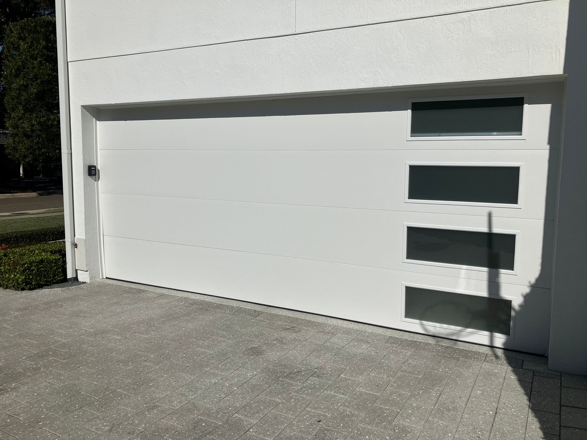 White garage door with four horizontal windows on the right side, set in a concrete driveway.