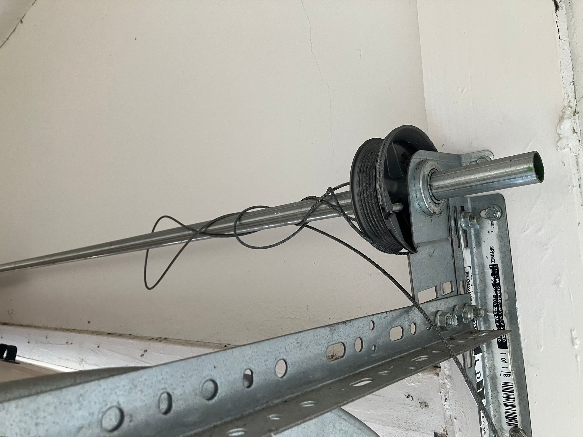 Garage door opener mechanism and track mounted on a ceiling, with cables and metal support braces.