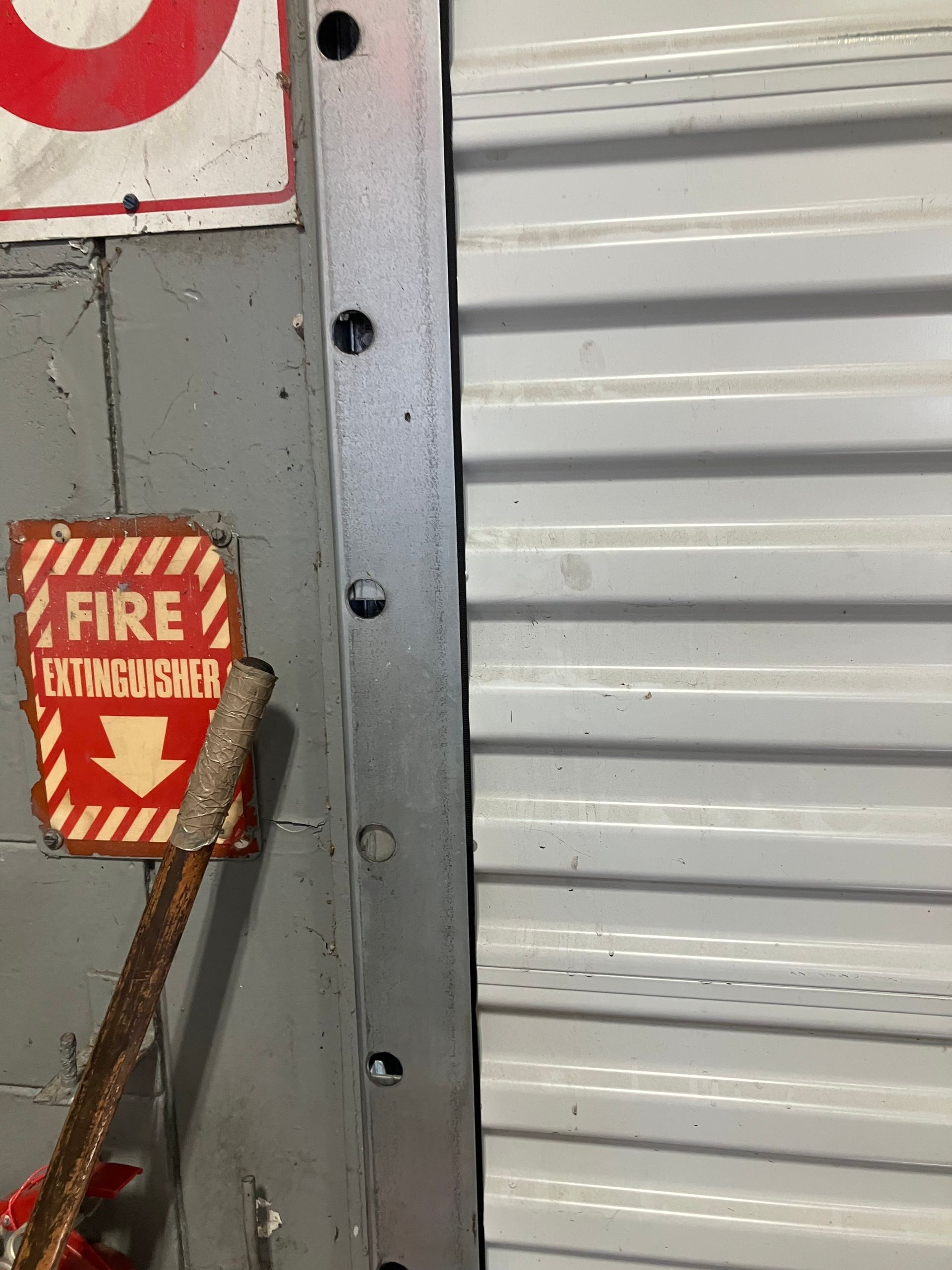 Fire extinguisher sign beside a metal garage door and gray wall.