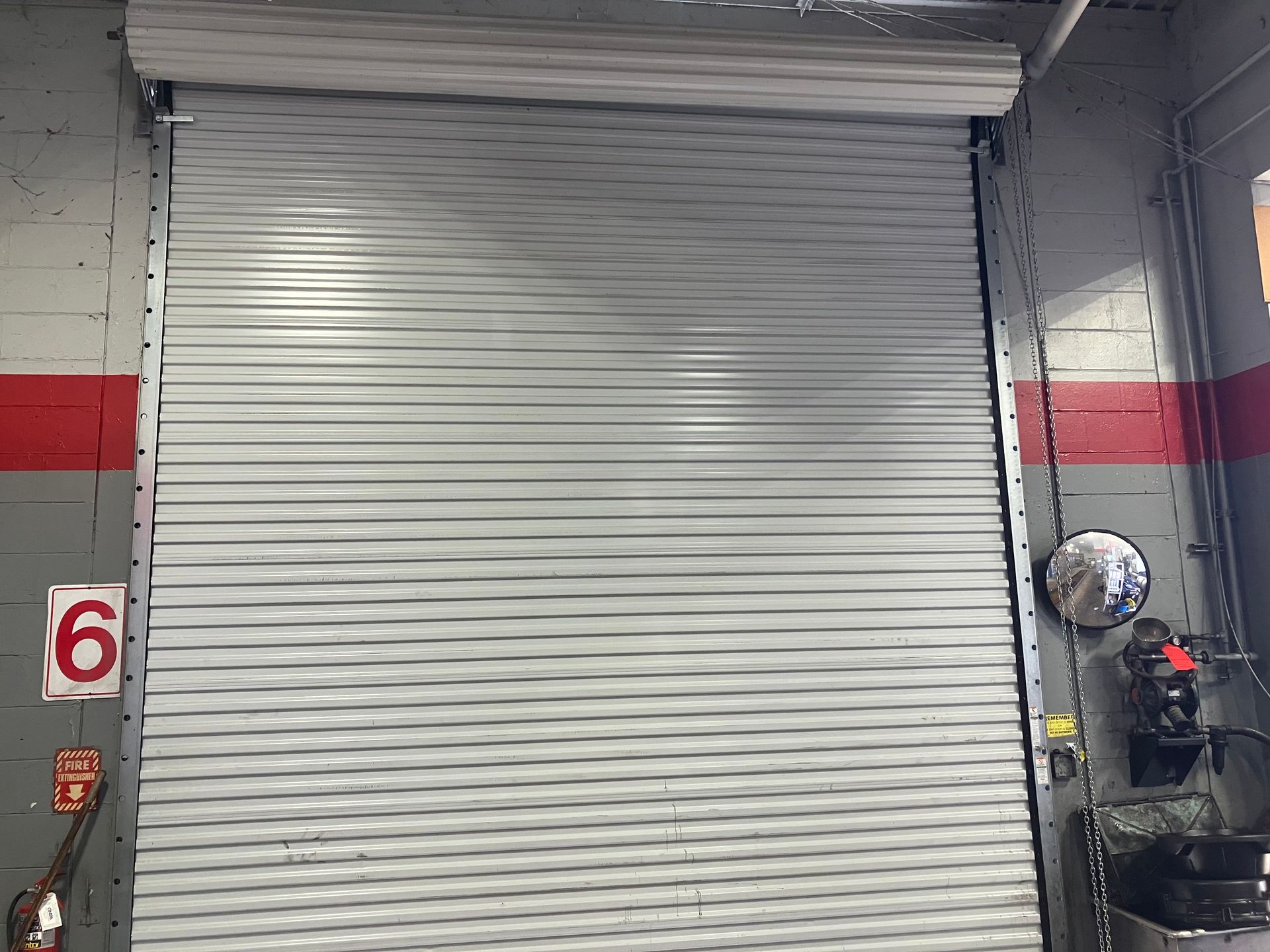 Closed gray metal roll-up garage door in an industrial bay with red and gray walls.
