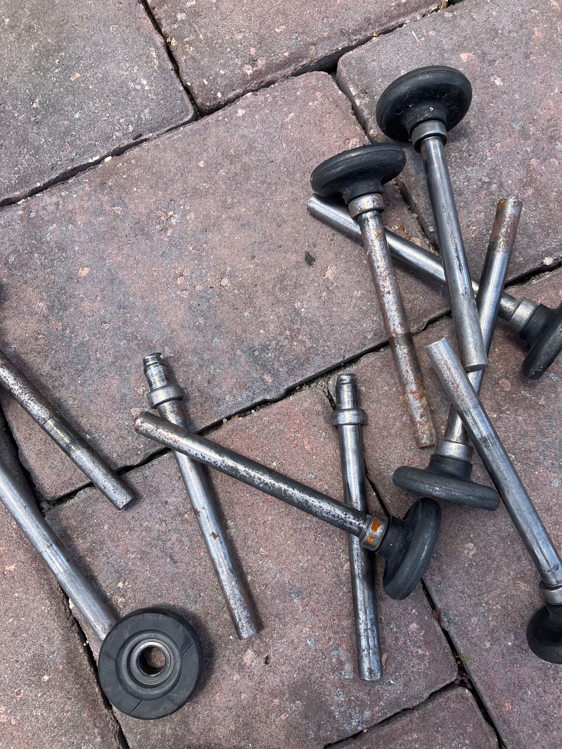 Scattered metal bolts with black rubber washers on a brick-paved surface.