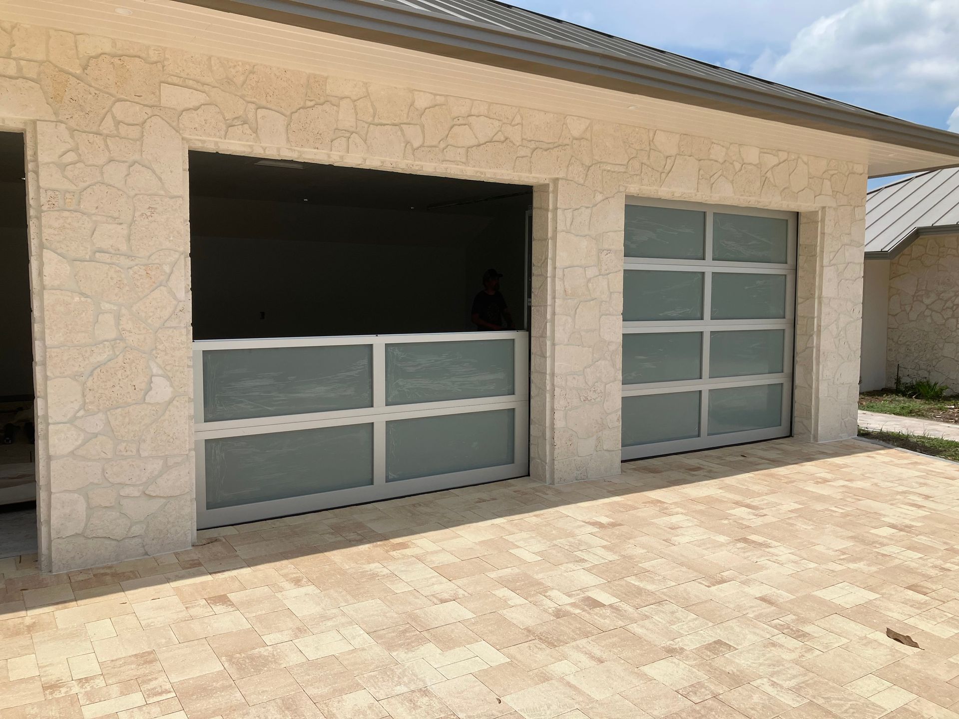 Beige stone house exterior with two modern glass garage doors and a paved driveway