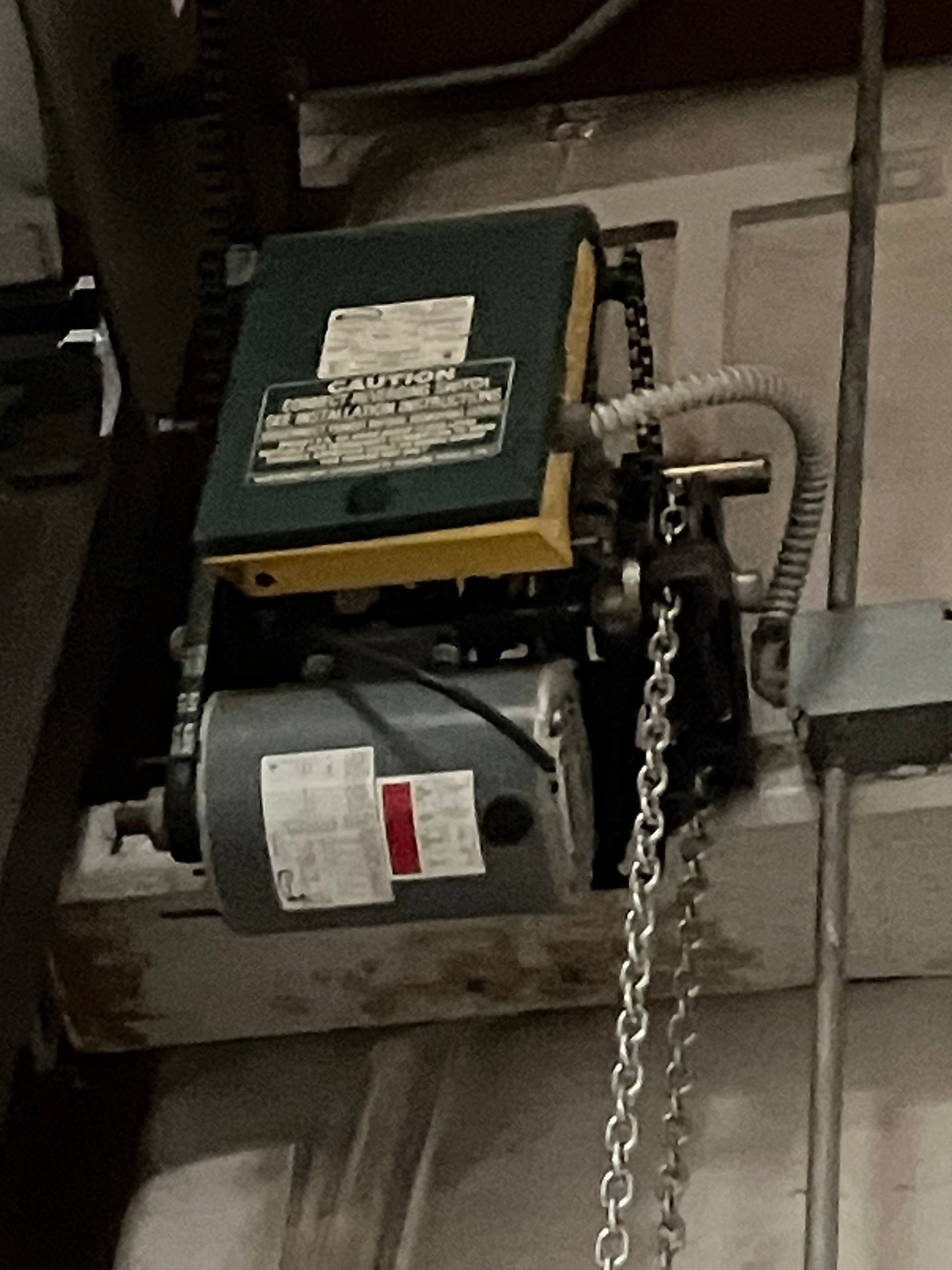 Electrical garage door opener with hanging chain and visible motor unit mounted to ceiling.