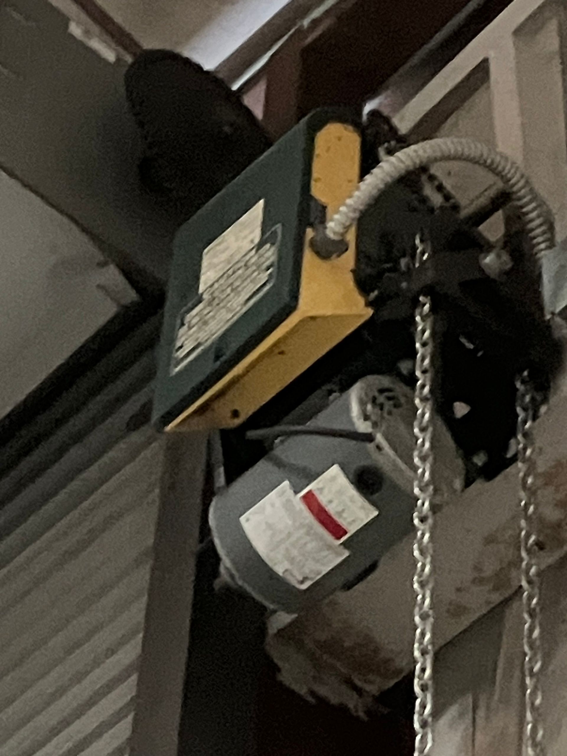 Garage door opener mounted near ceiling, with chain, motor, and yellow housing