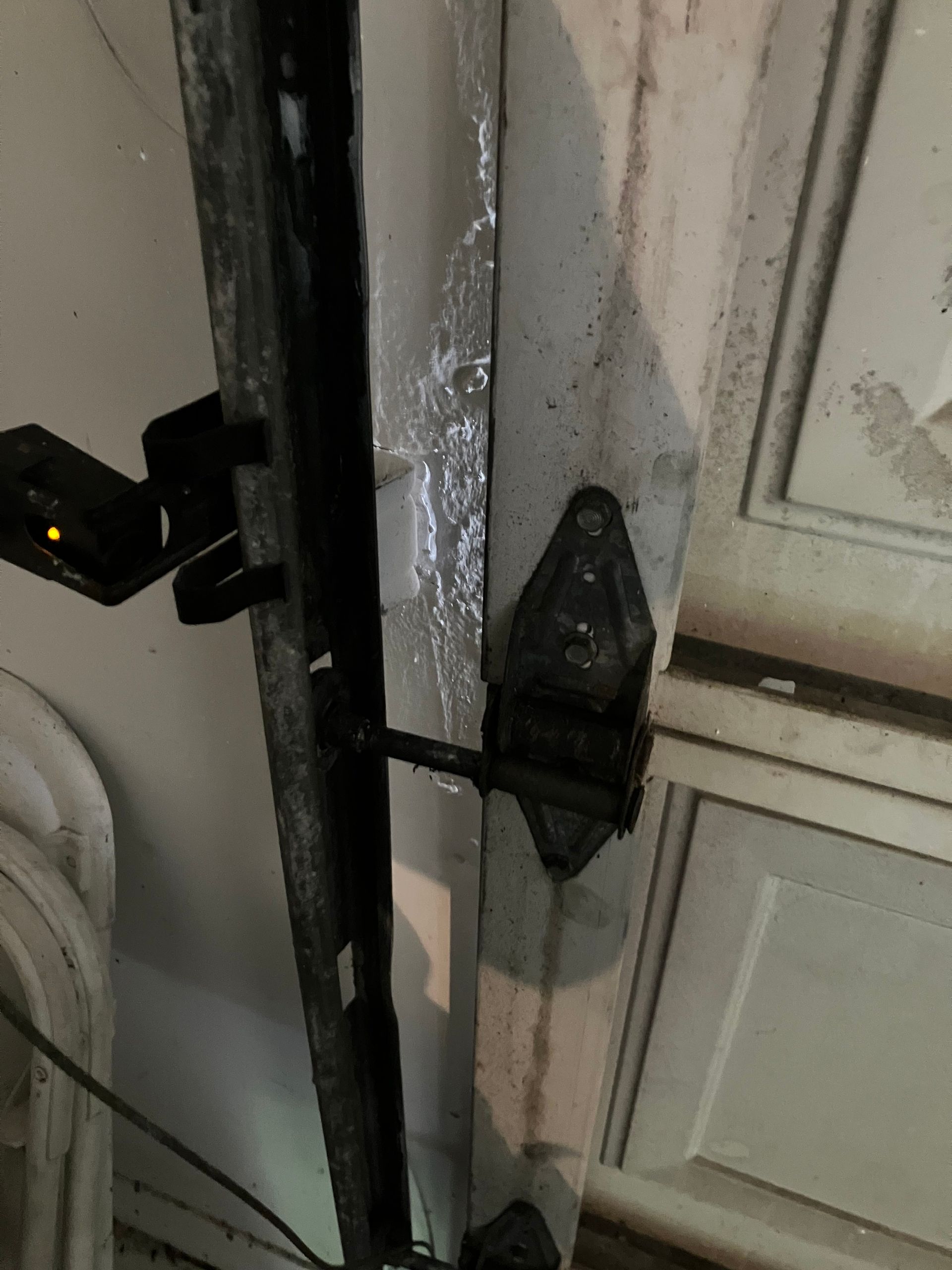 Black metal latch securing a white cabinet door, with a small device clipped to the left side.