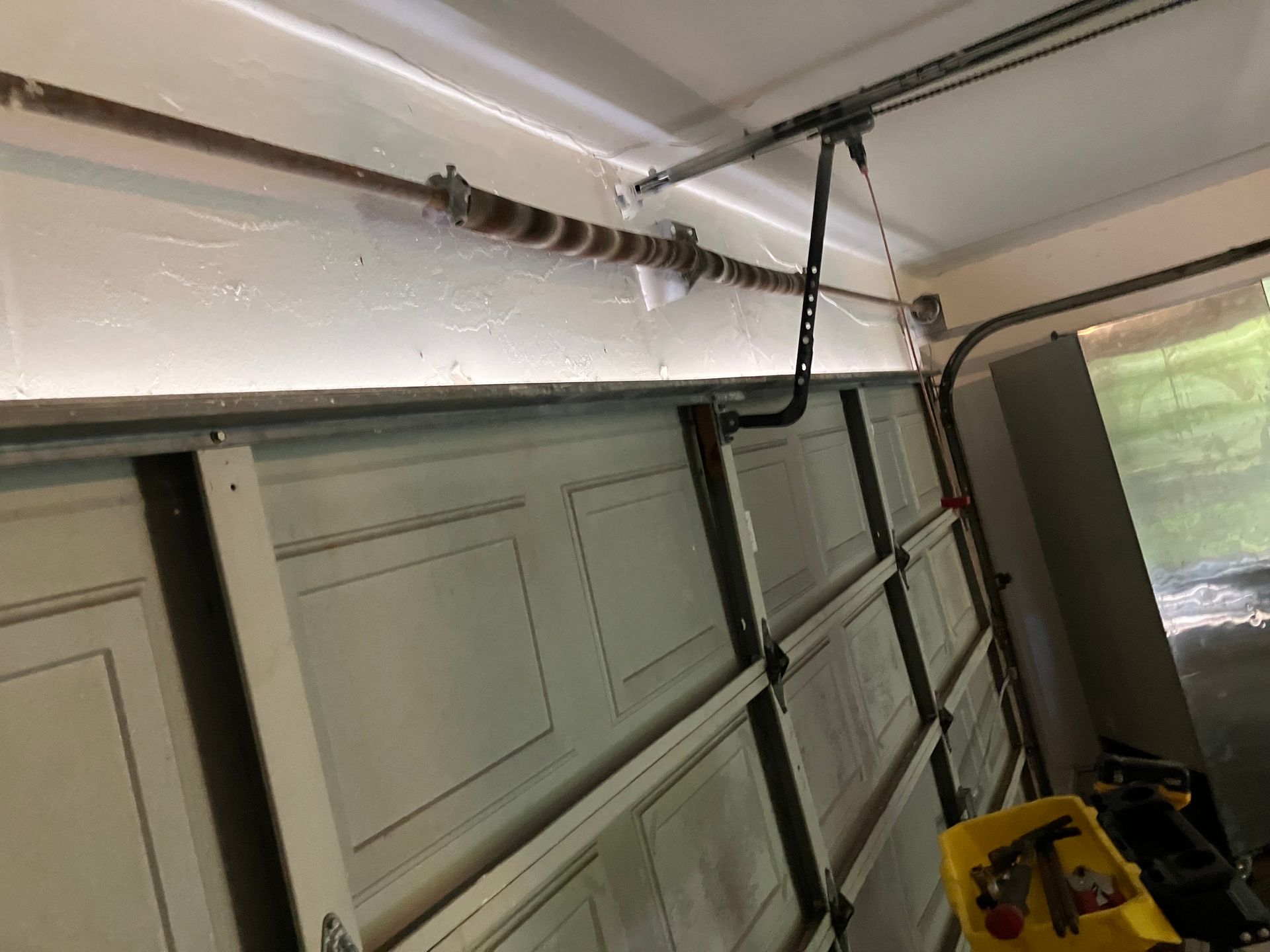 Interior of a garage with an open overhead door, door tracks, and a yellow step stool under a white ceiling.