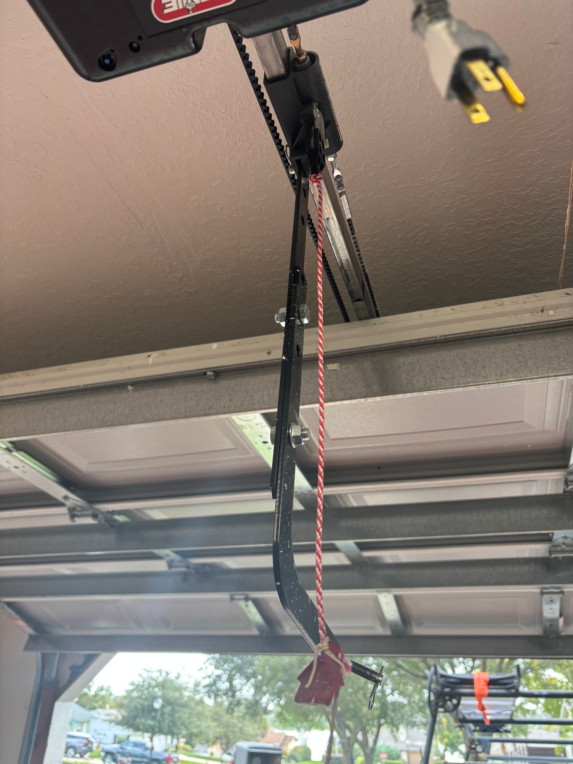 Garage door opener hanging from ceiling with exposed wires and a red cord.