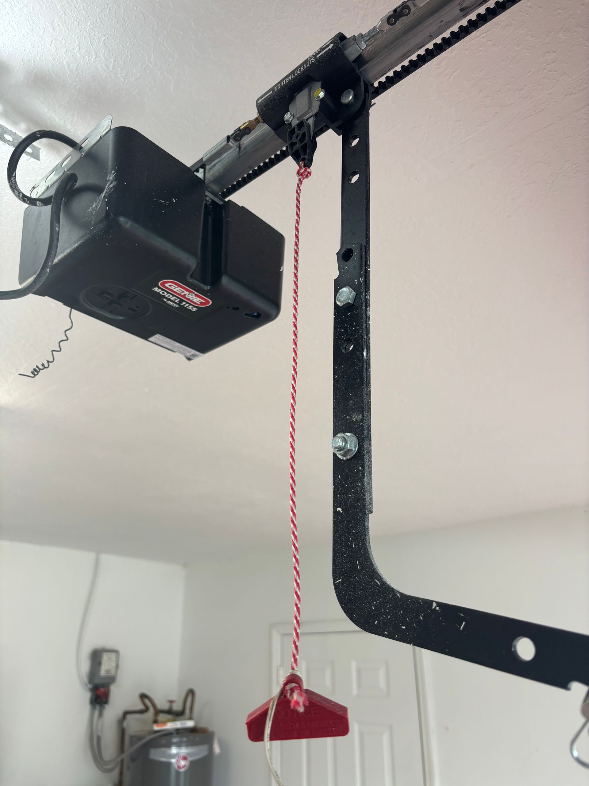 Garage door opener with a red emergency release cord hanging from the rail and motor unit.