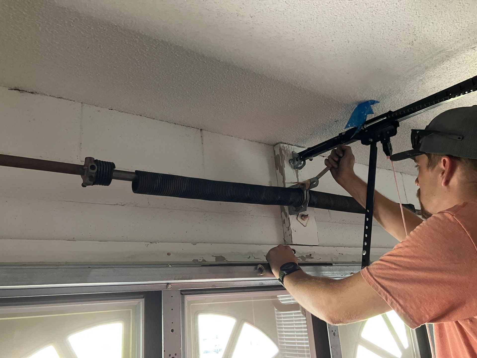 Person using a tool to install a ceiling-mounted garage door opener above a window.