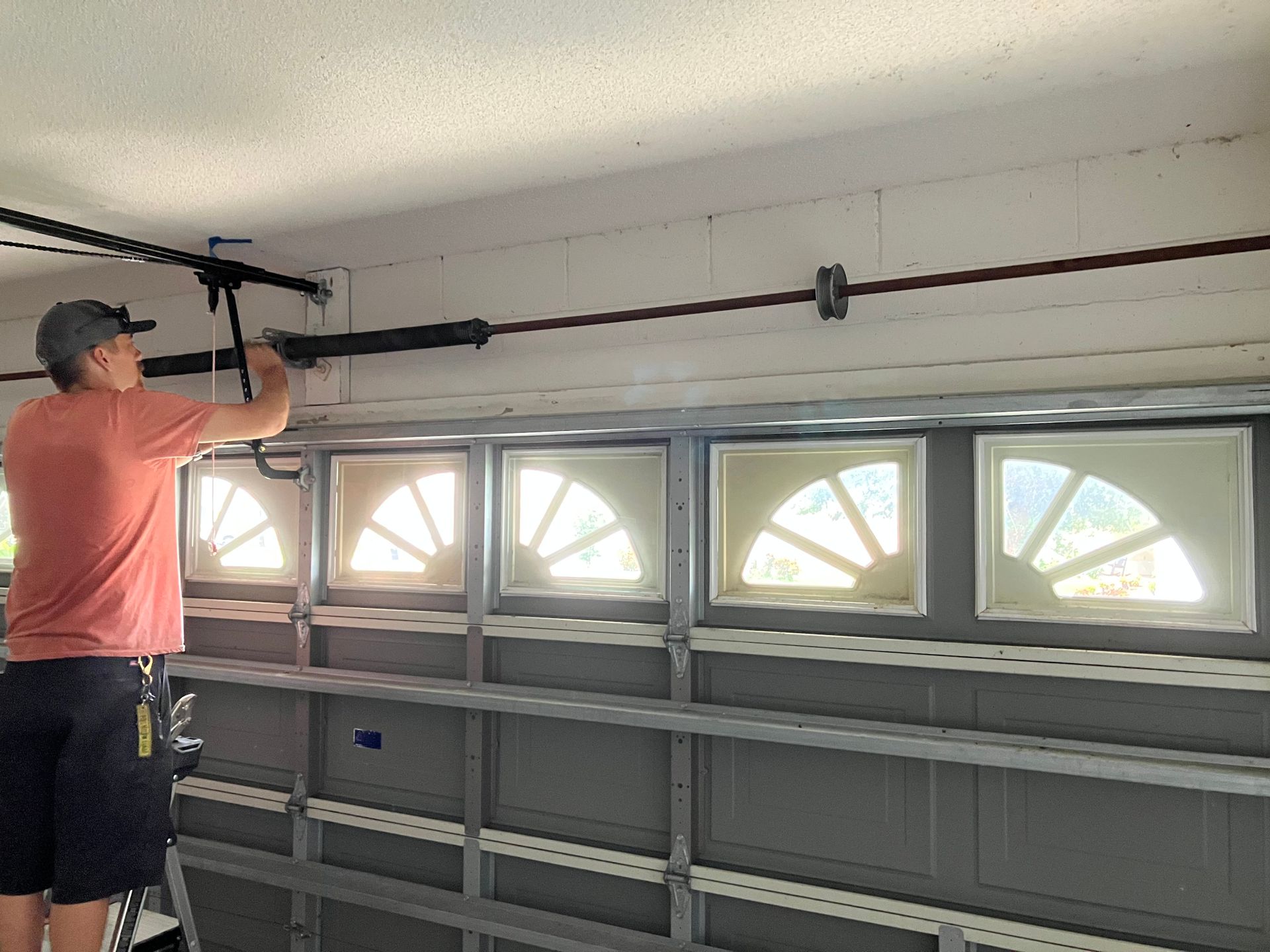 Person adjusting a garage door opener rail in a garage with windows along the door.