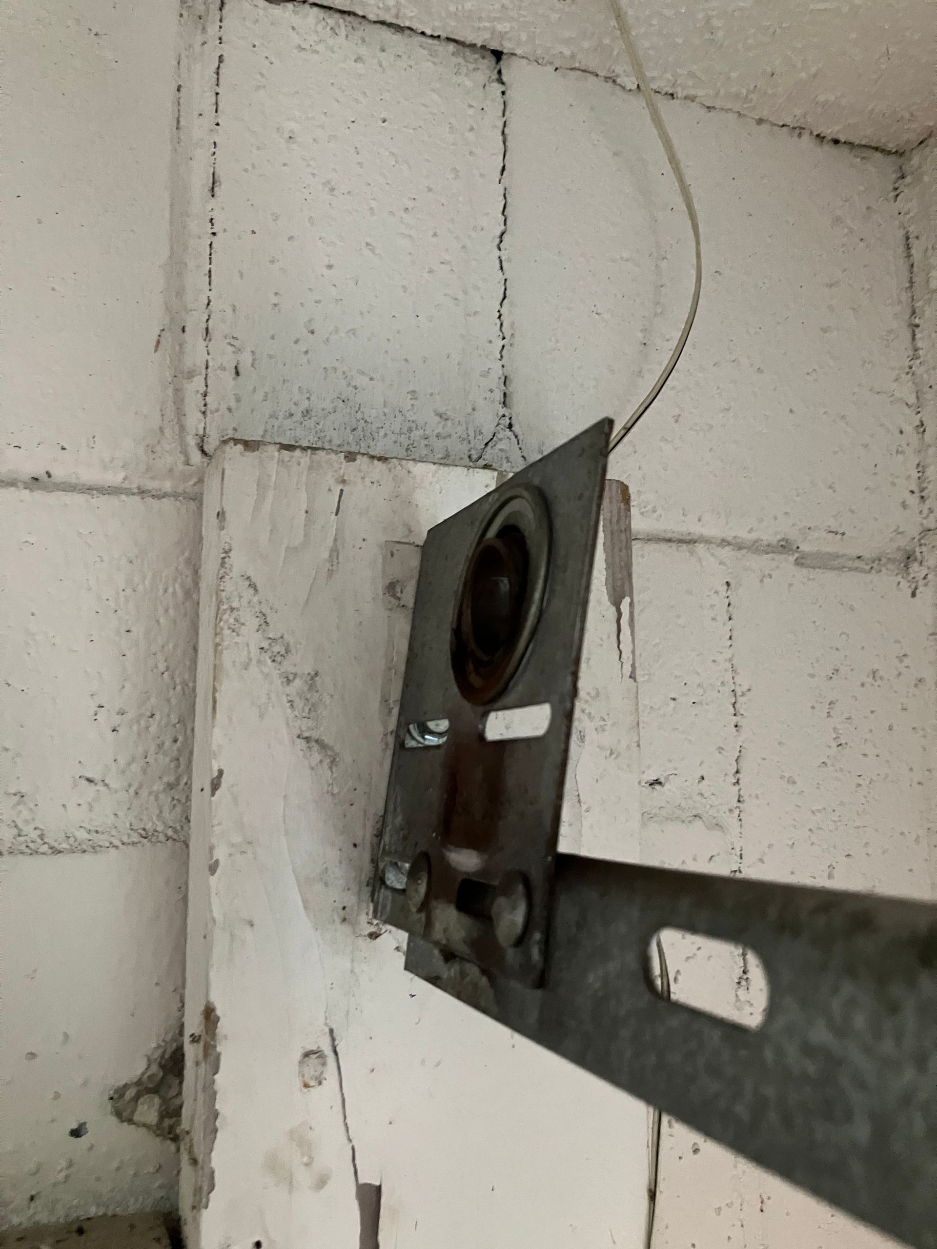 Metal wall bracket mounted on a white cinder block wall with a loose cable hanging above it
