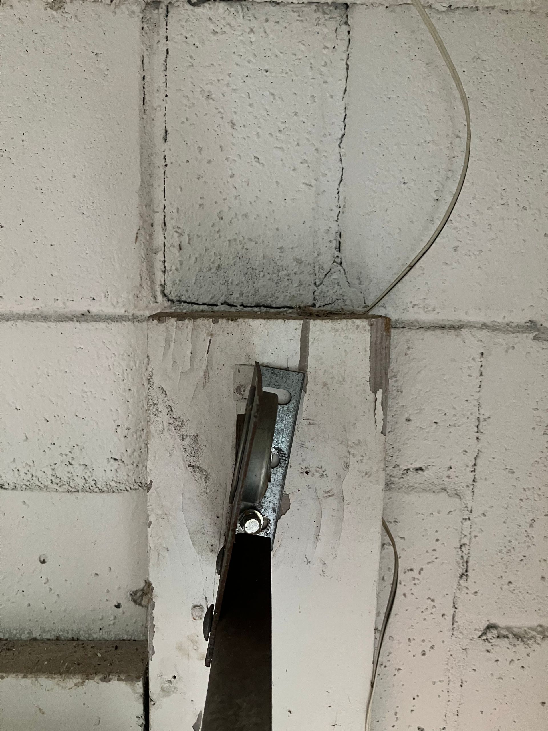 Damaged concrete wall with a jagged hole and exposed metal bracket.