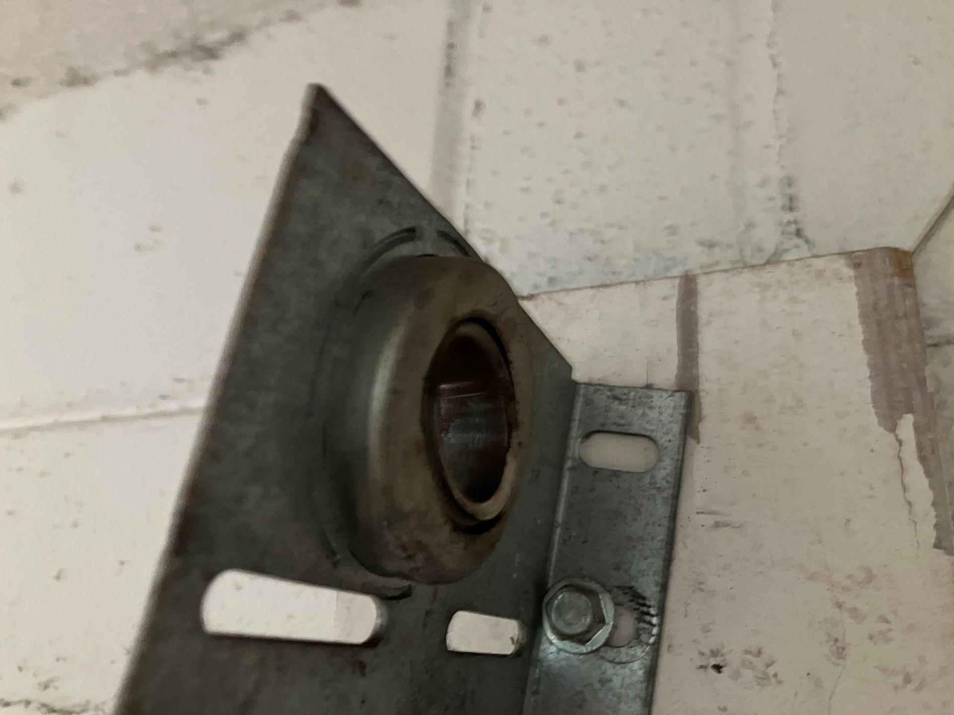 Close-up of a metal wall bracket with an empty round opening on a painted cinderblock wall