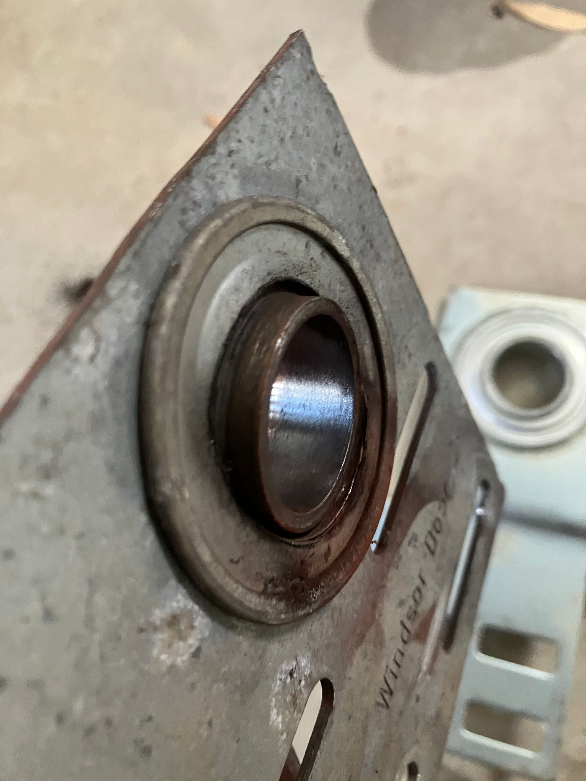 Close-up of a worn metal bearing mounted on a gray bracket.