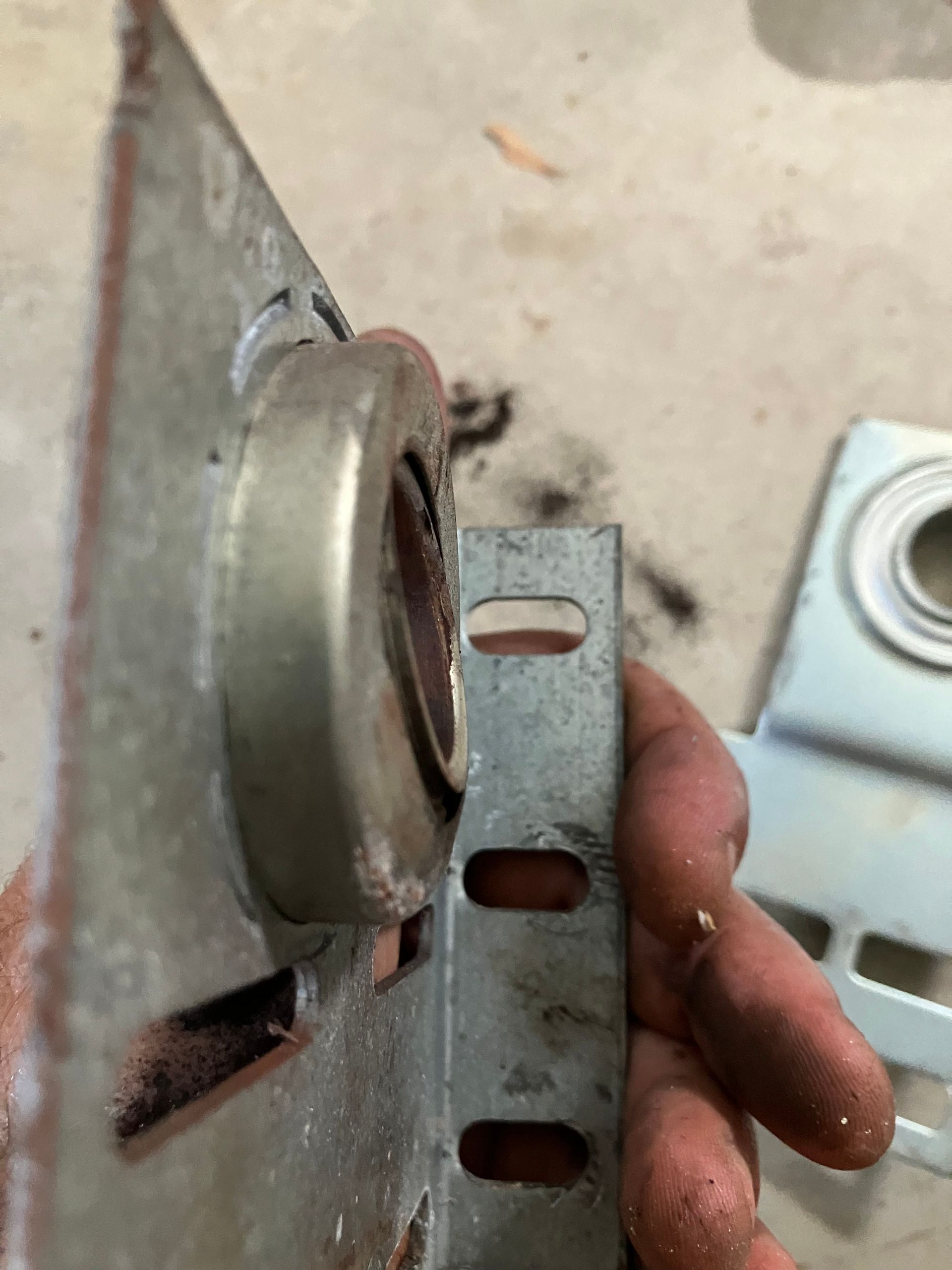 Close-up of a hand holding a perforated metal bracket next to a round wall-mounted fixture.