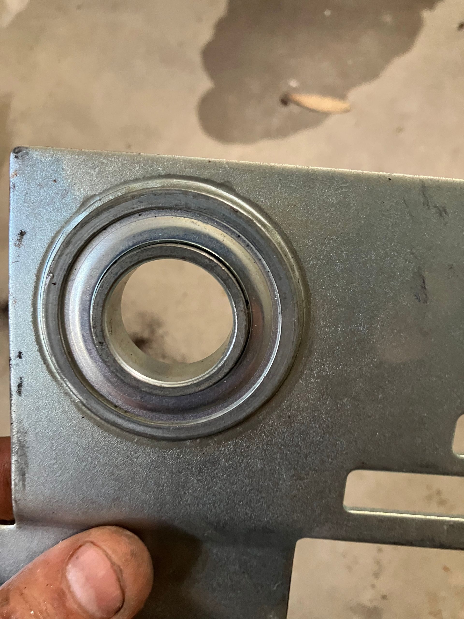 Close-up of a metal bracket with a circular bearing opening and a hand holding the edge.