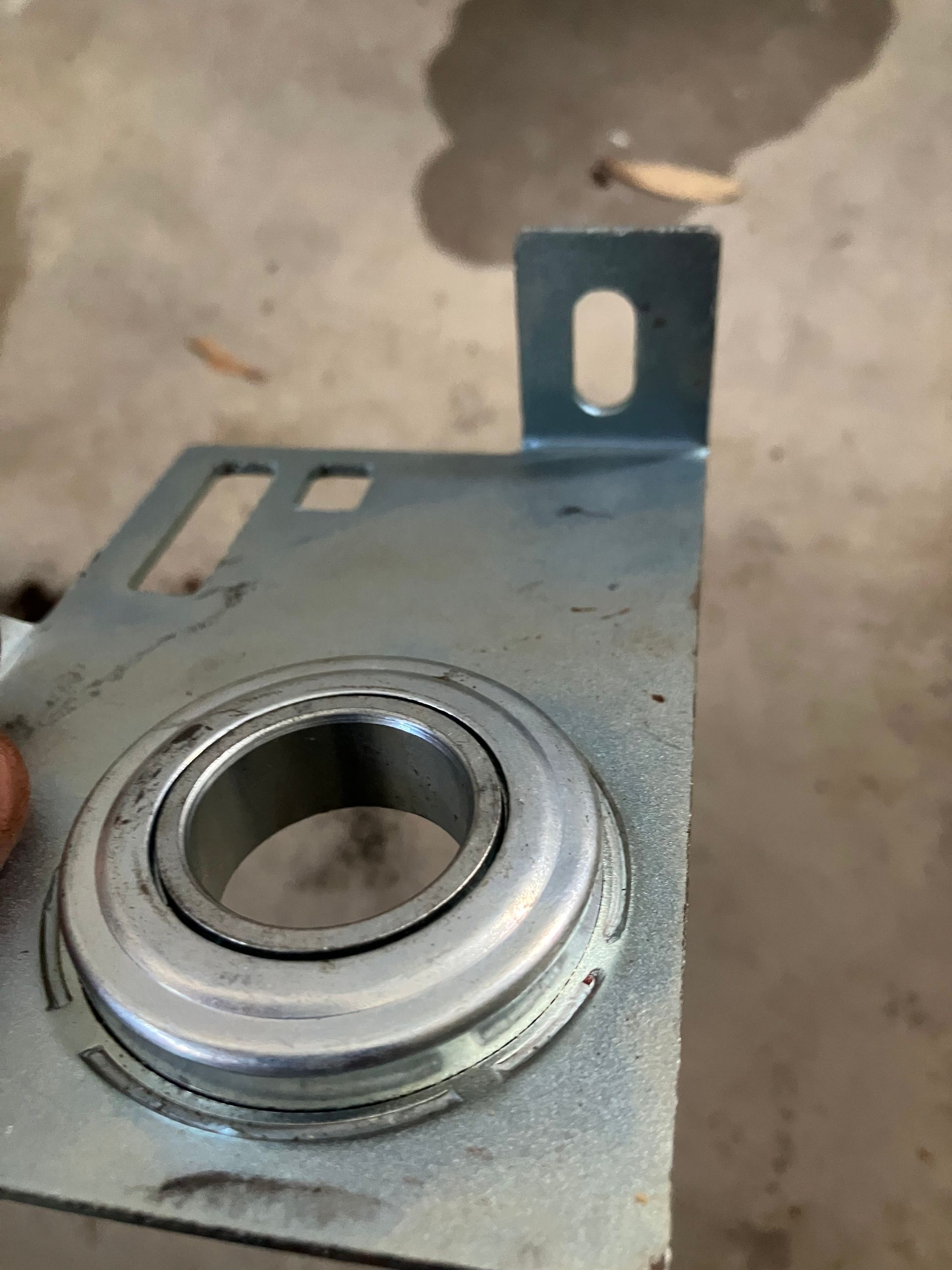Close-up of a metal bracket with a circular bearing mount and slotted tab.
