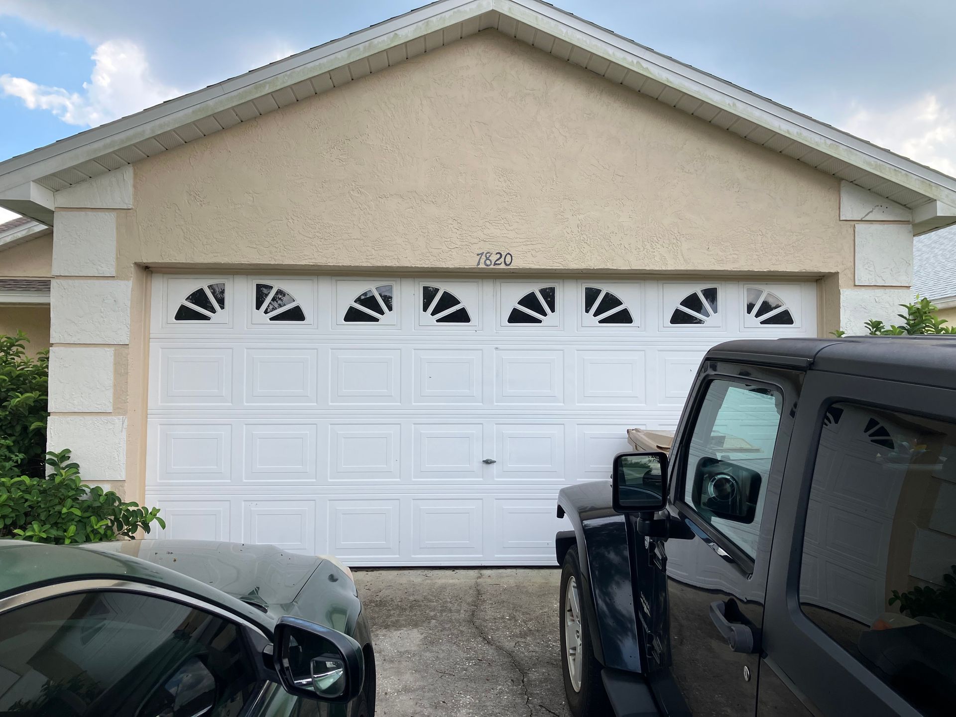 White garage door on a suburban house, with a black SUV and car parked in the driveway.