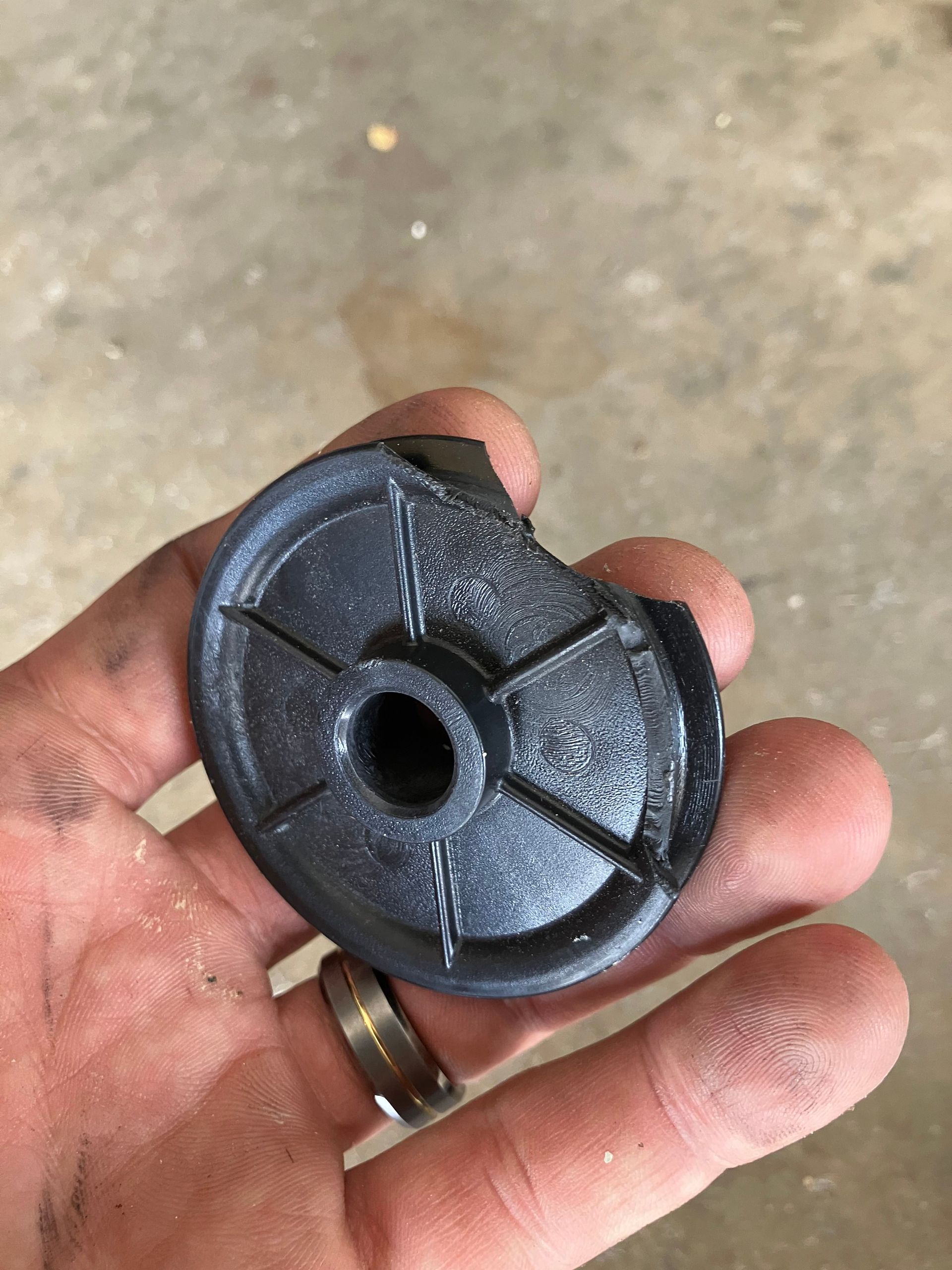 Hand holding a black circular plastic part with a center hole and split seam.