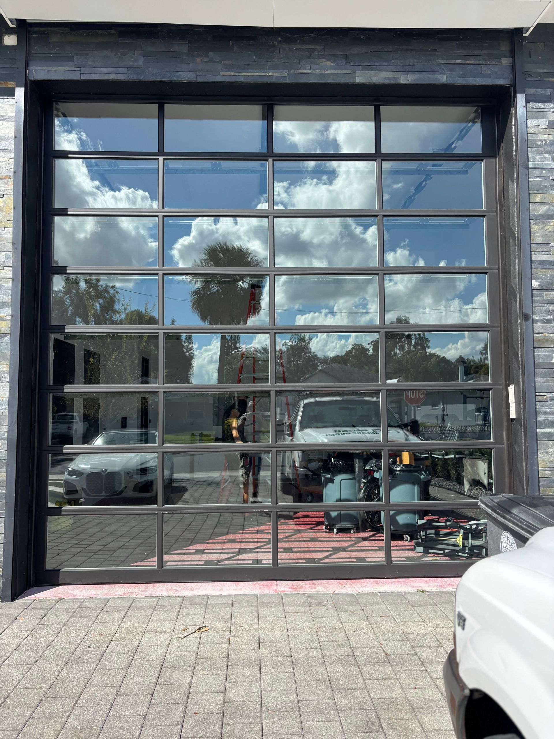 Glass-front storefront reflecting blue sky and clouds, with parked cars visible outside.