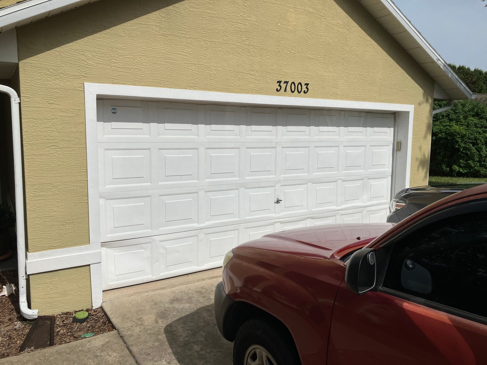 White garage door on beige house with black house number, red SUV parked in foreground.