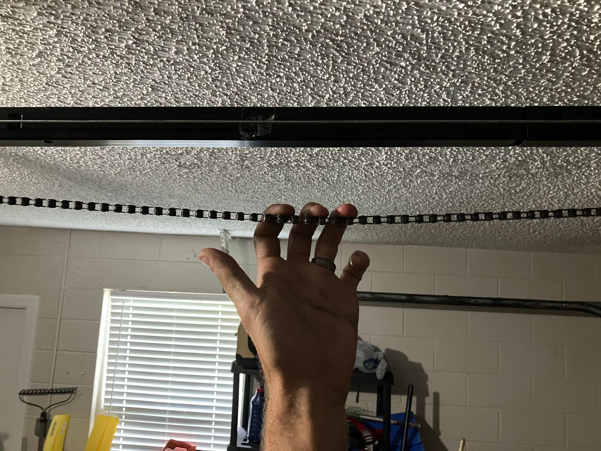 Hand reaching up toward a speckled ceiling, with window blinds and shelves in the background