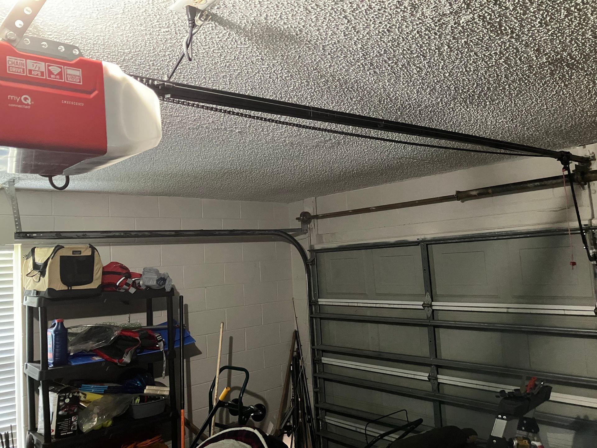 Garage interior with speckled ceiling, open garage door, shelving, tools, and a red garage door opener.