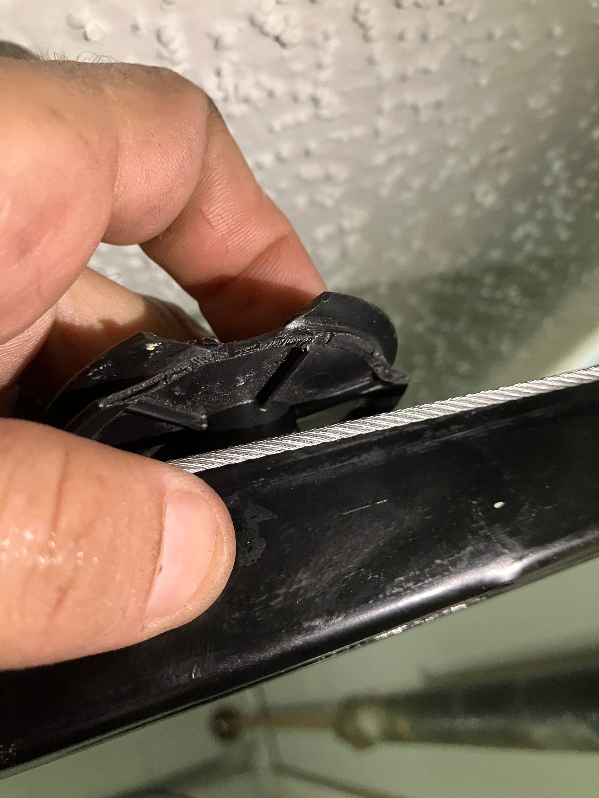 Hand holding a black plastic object with a torn seam or broken clip close to a textured white surface