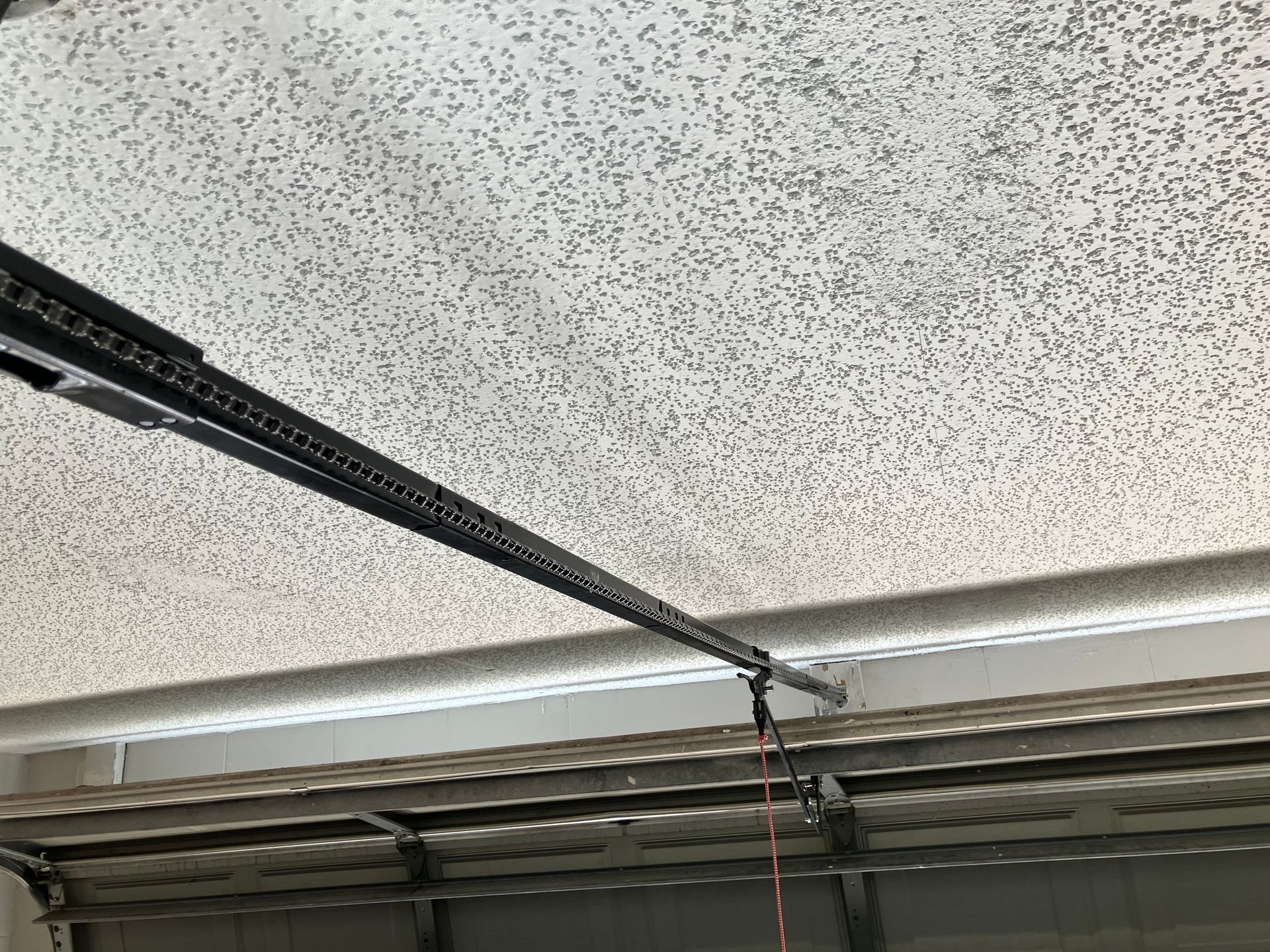 Garage door opener rail mounted to a textured ceiling with a hanging cord