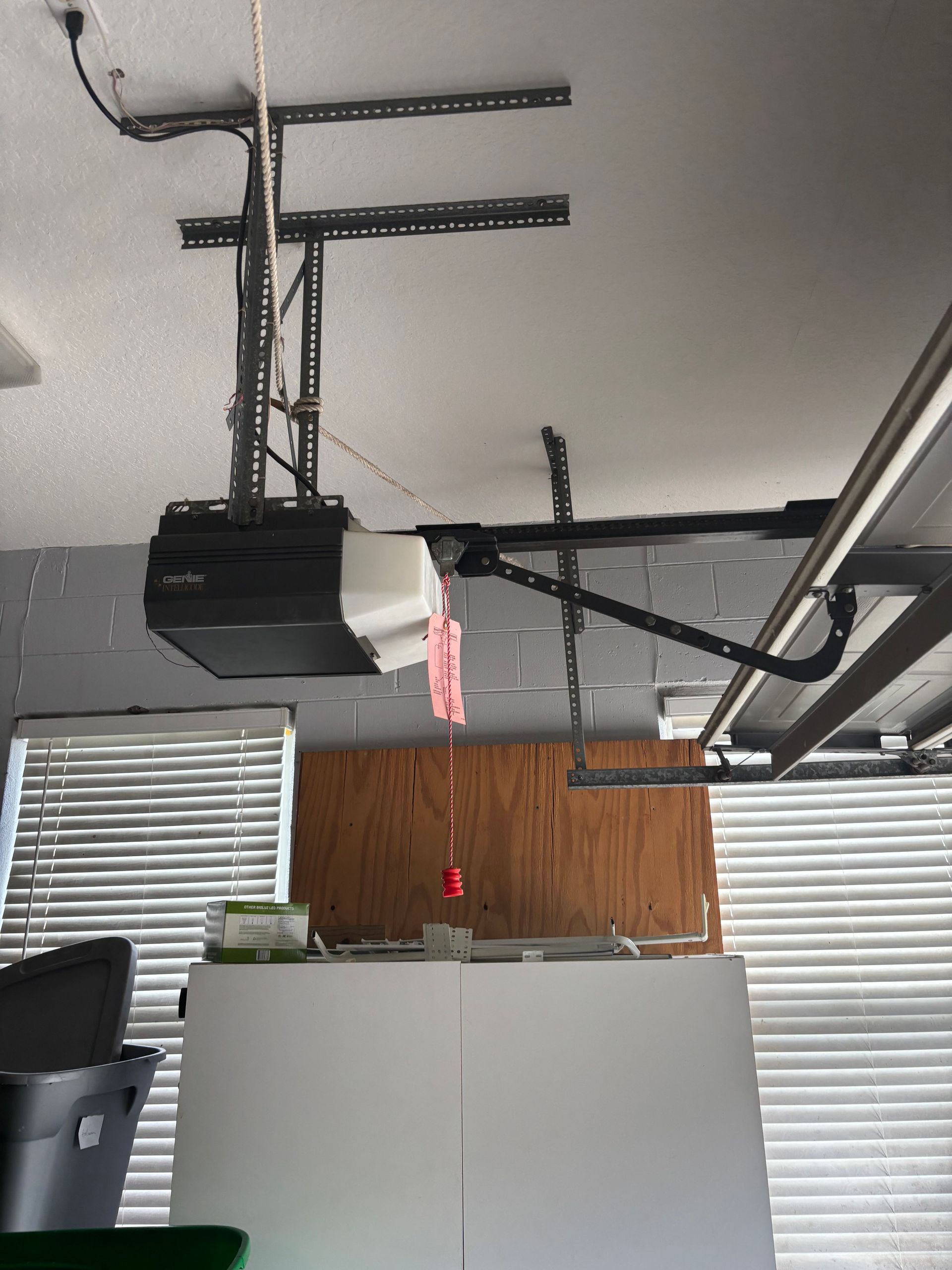 Garage with an overhead door opener, exposed tracks, white cabinets, and a wood-paneled wall above blinds