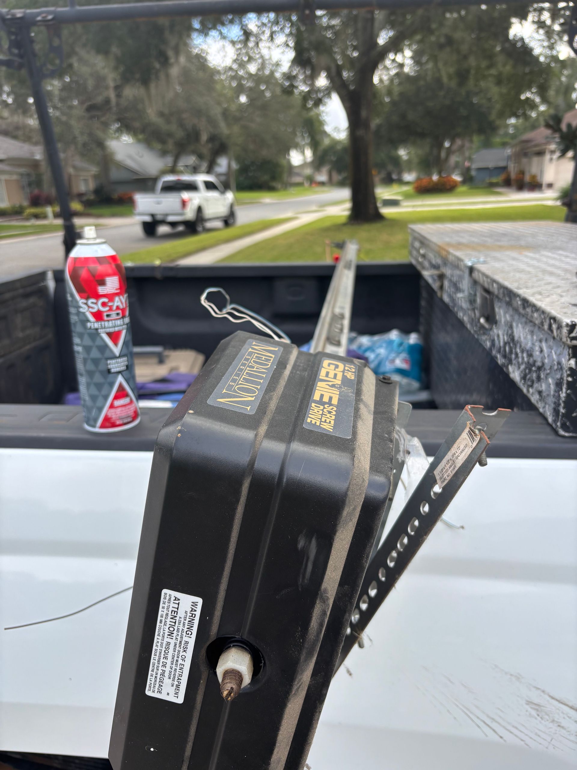 Black suitcase standing on a truck bed beside a red can, with a suburban street in the background.