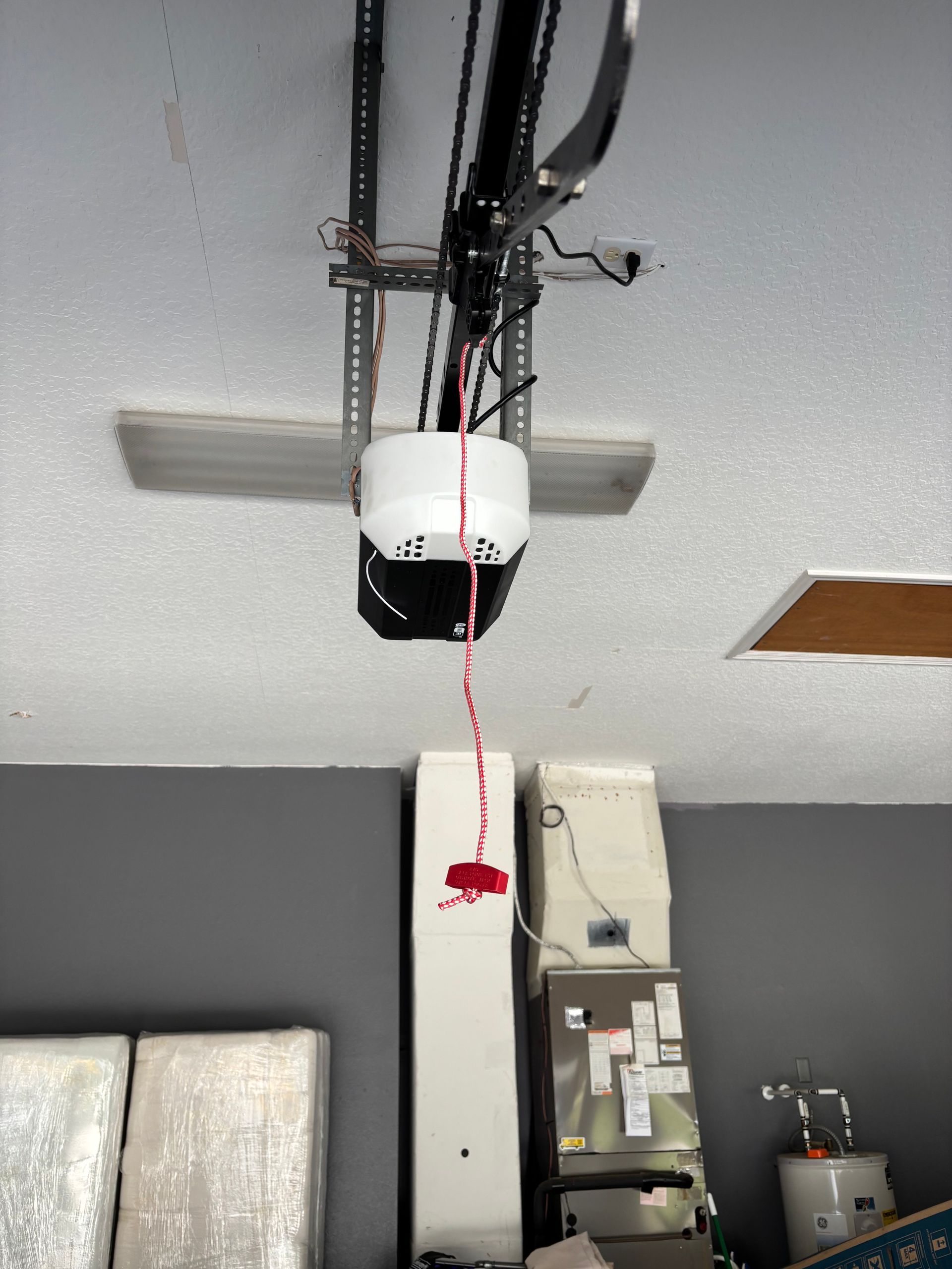 Garage ceiling with a white automatic door opener and hanging cord above storage cabinets.