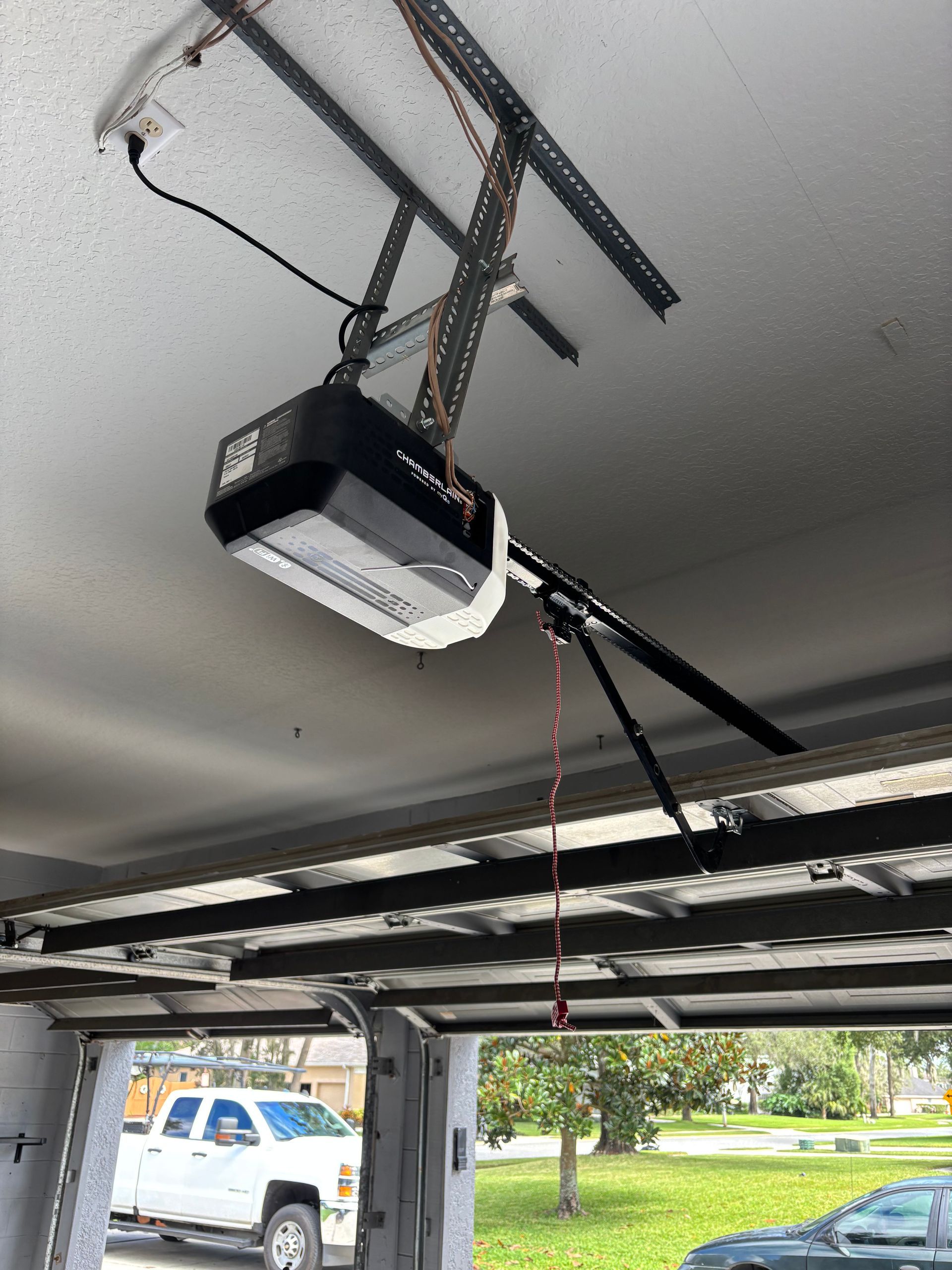 Garage door opener hanging from the ceiling with the garage door open and a red pull cord.