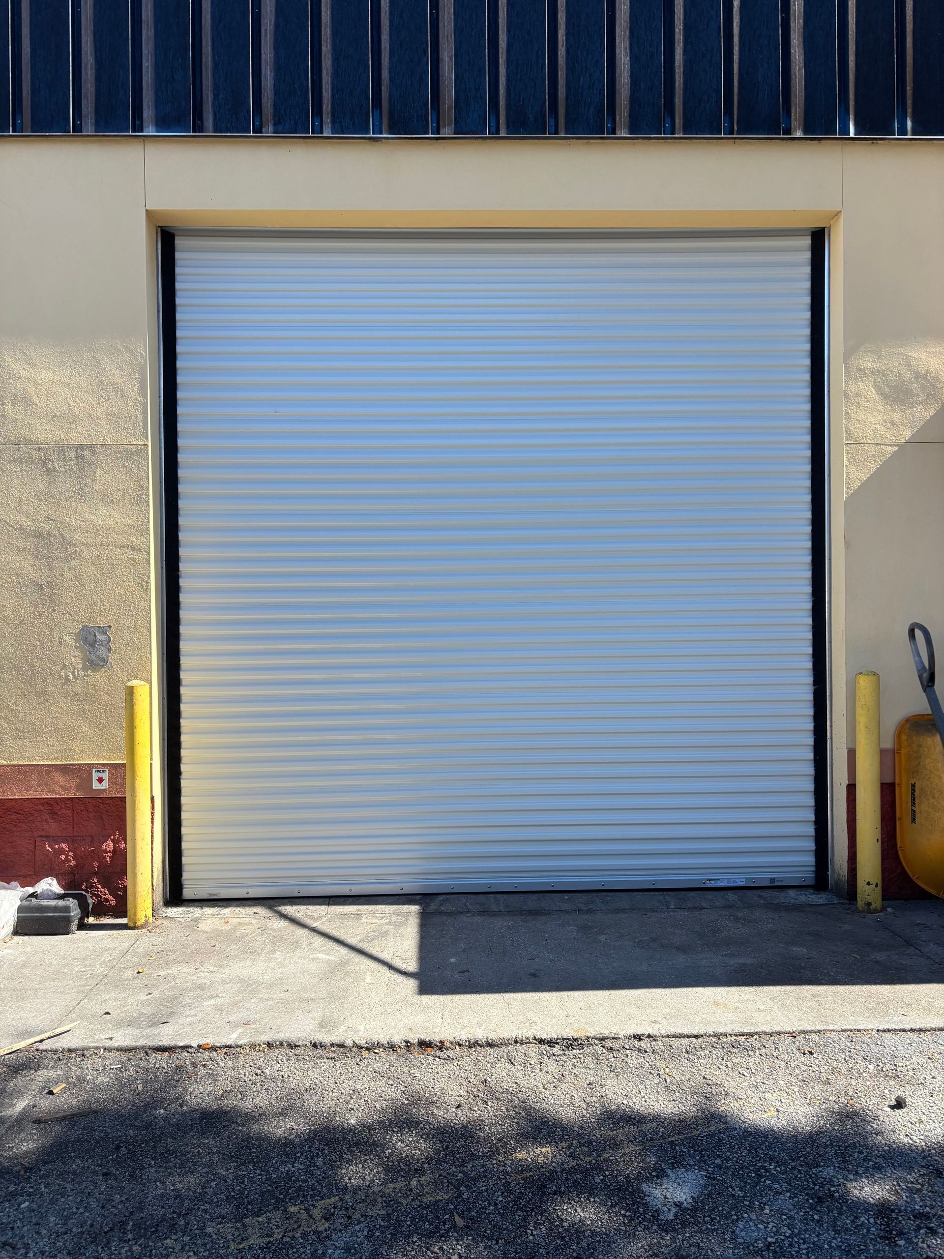 Closed gray roll-up garage door on a warehouse exterior in sunlight