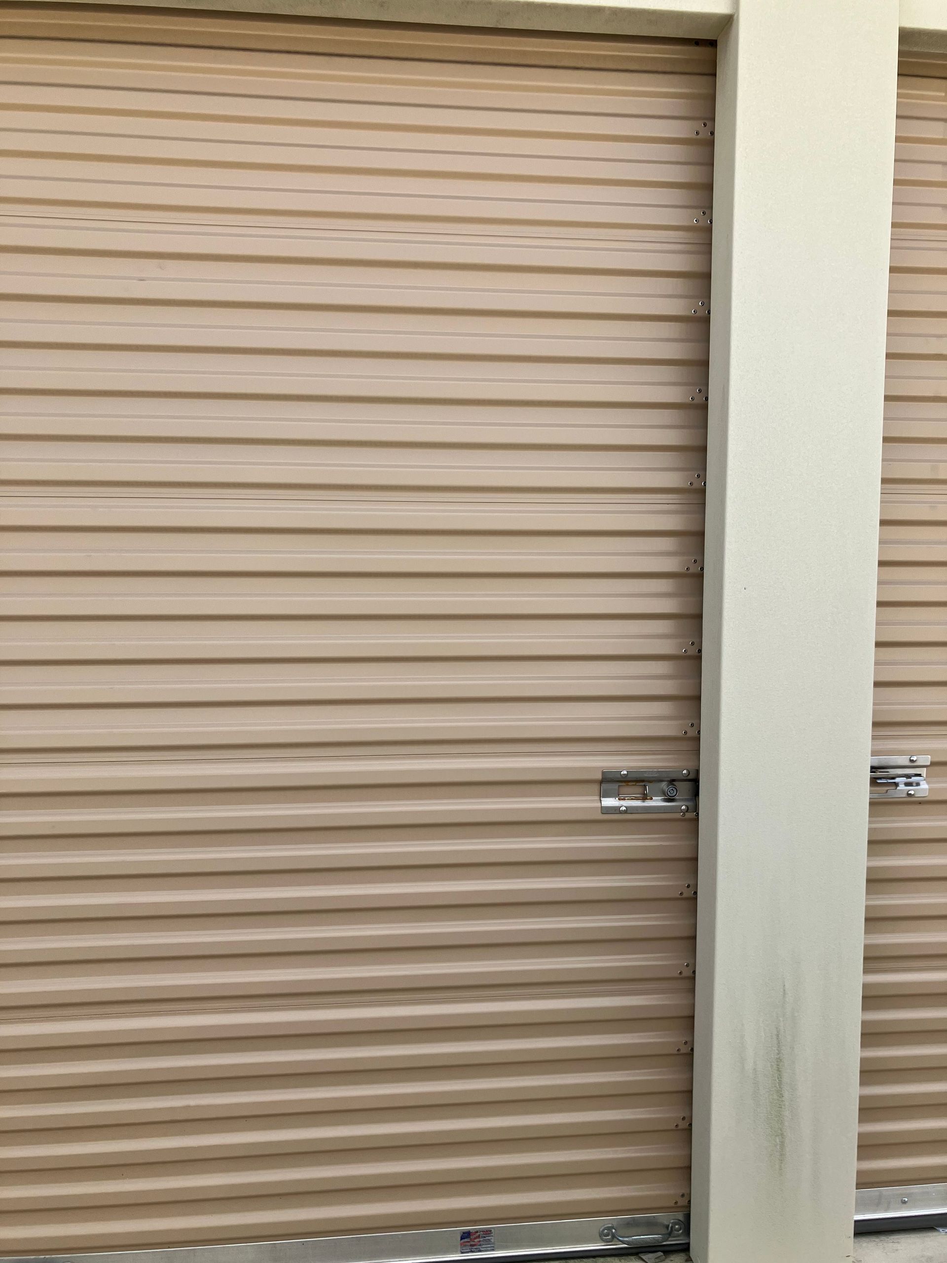 Beige metal roll-up door with horizontal slats and a silver latch, beside a white wall.