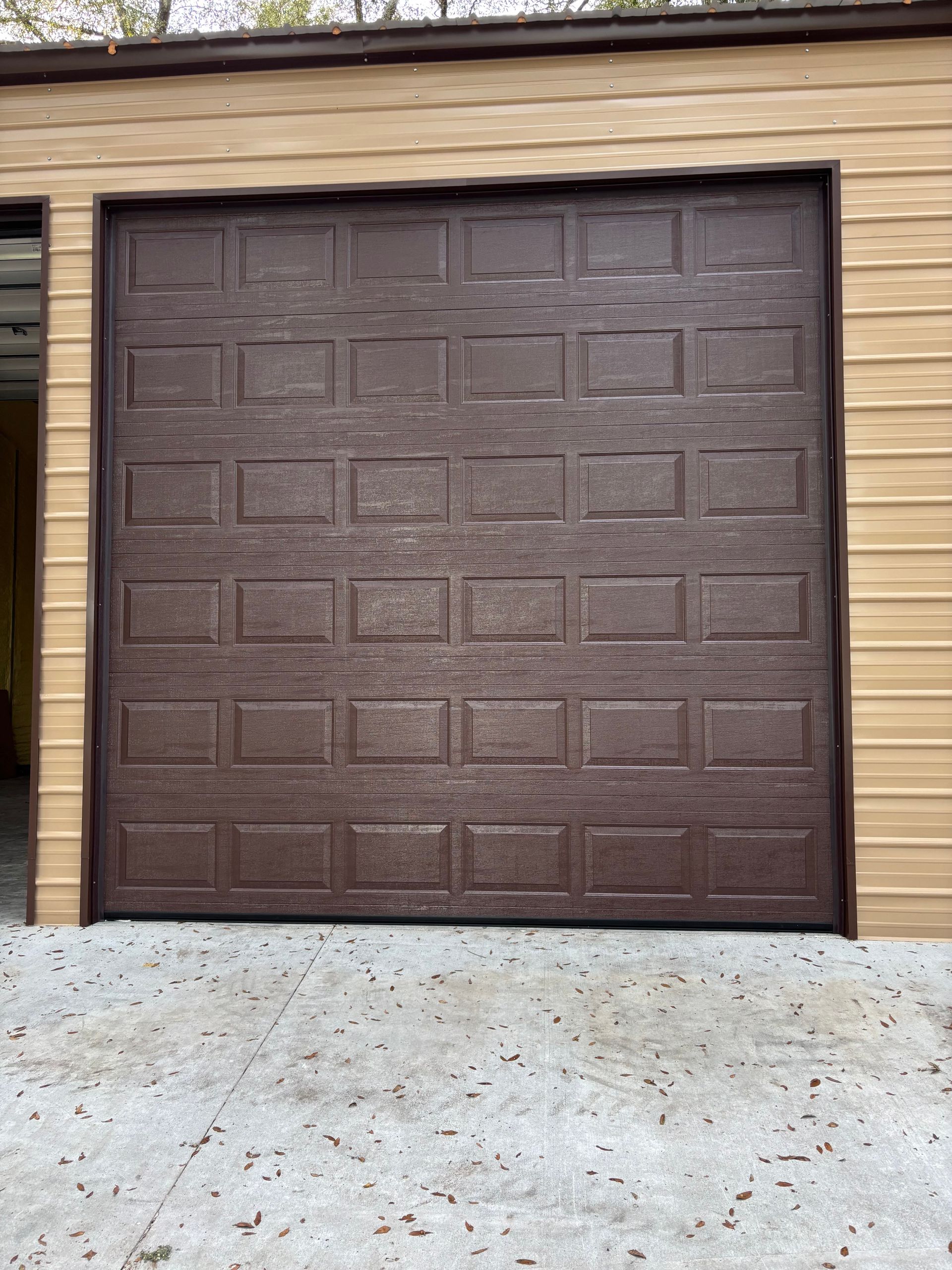 Brown garage door with rectangular panels on a beige-sided house above a concrete driveway