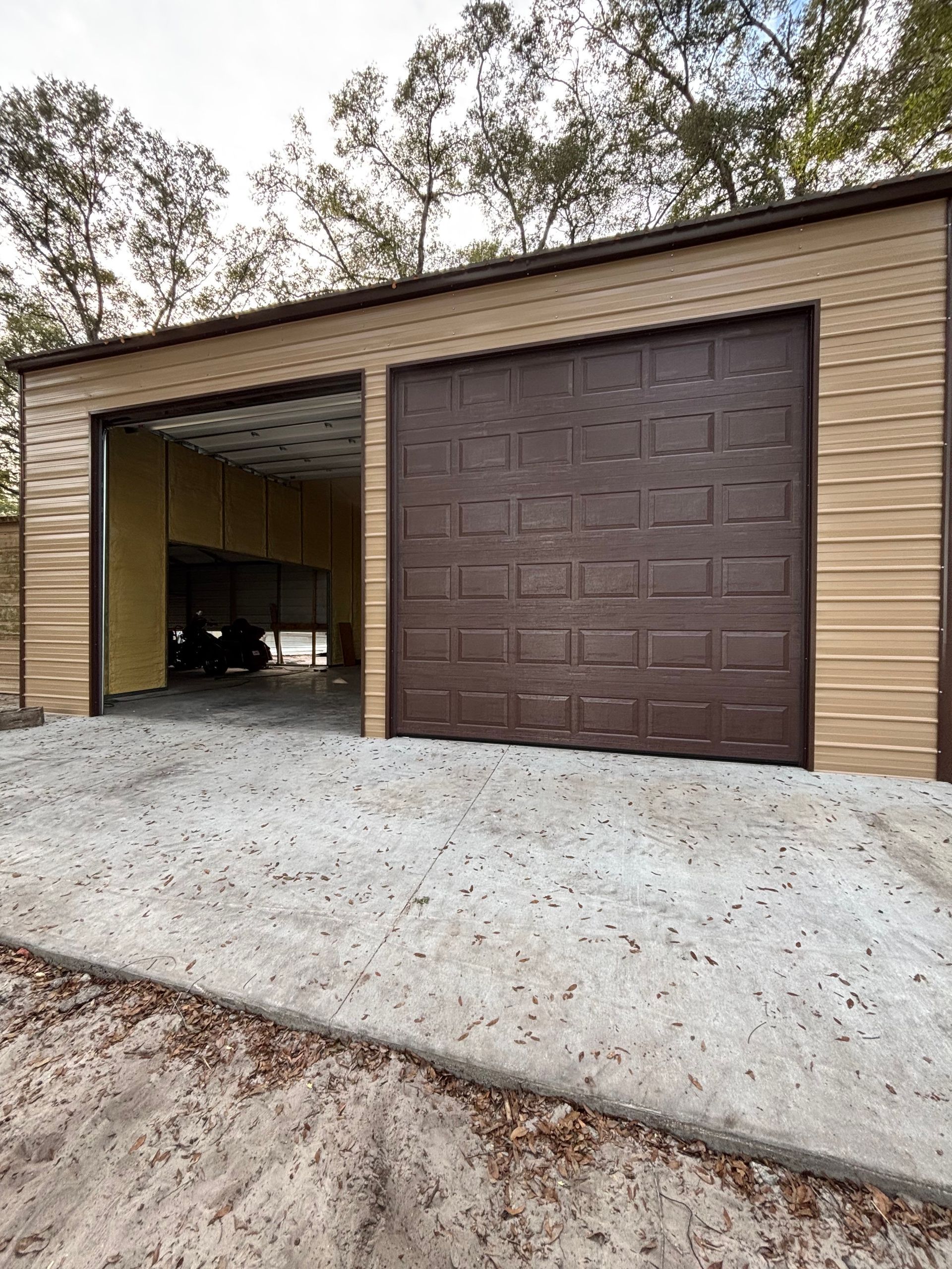 Two-car garage with brown doors and a concrete driveway, one door open to a dark interior.