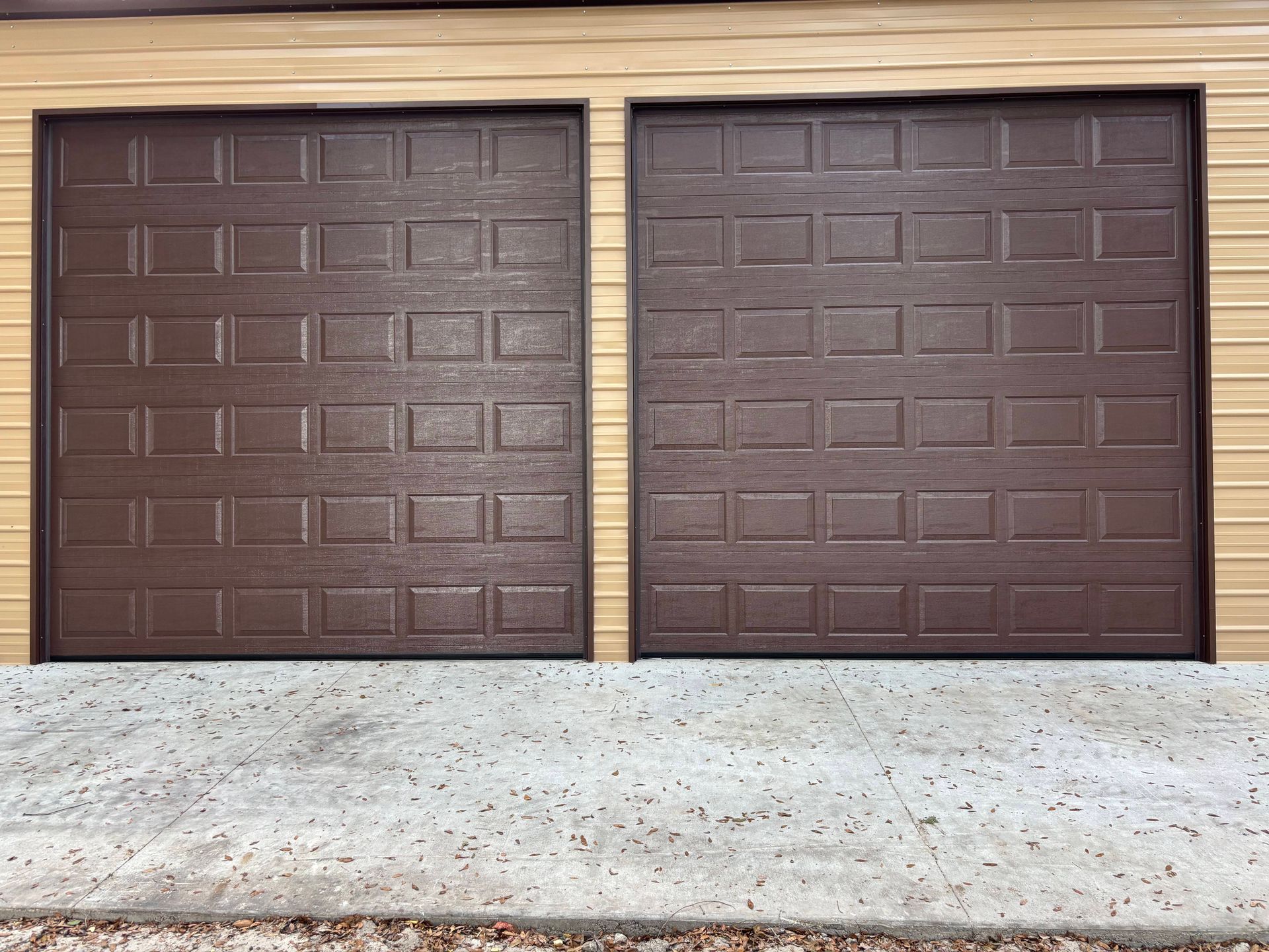 Two brown garage doors on a beige exterior wall above a concrete driveway.