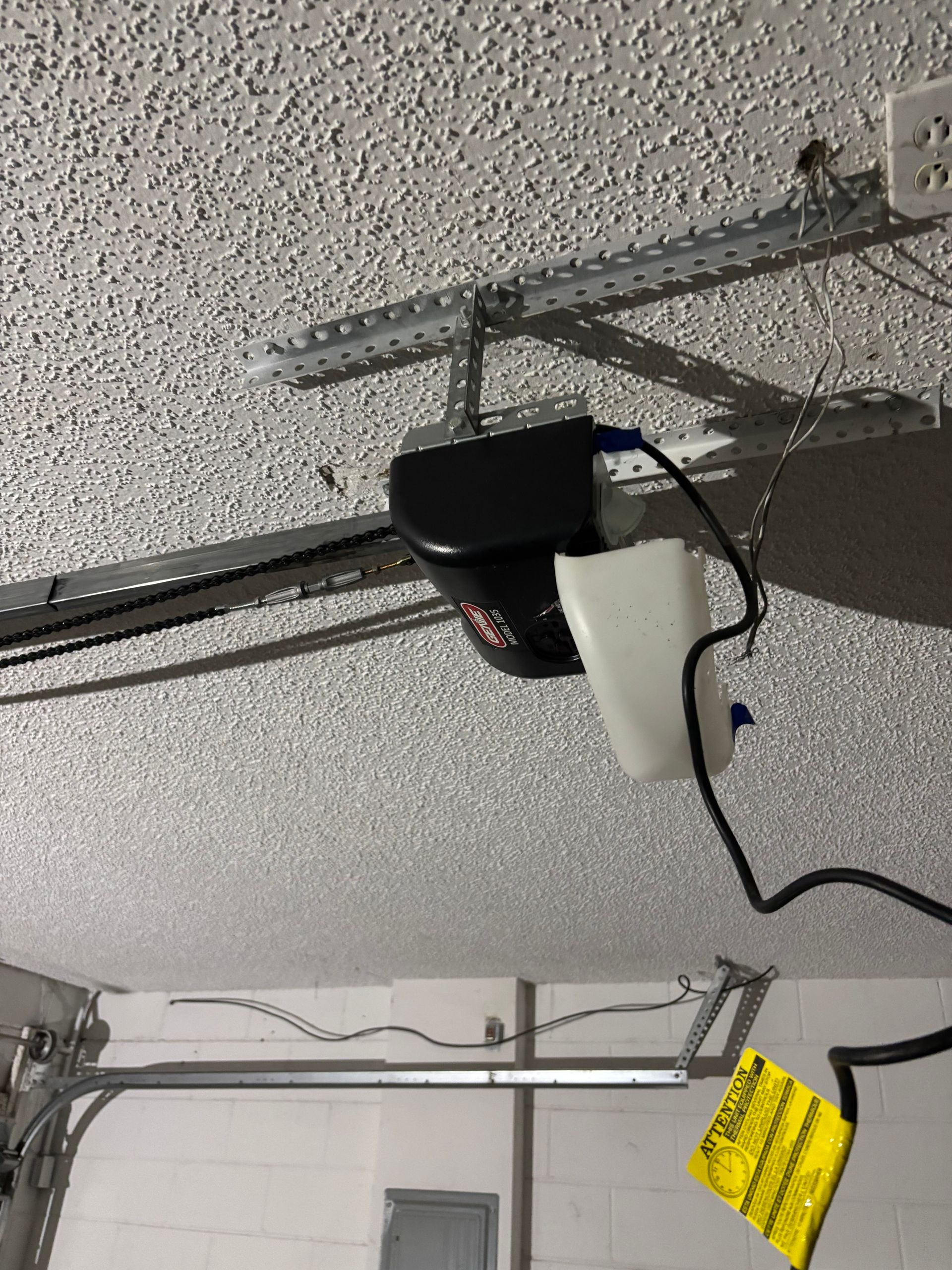 Garage ceiling with a mounted black device and hanging cable on a metal track.