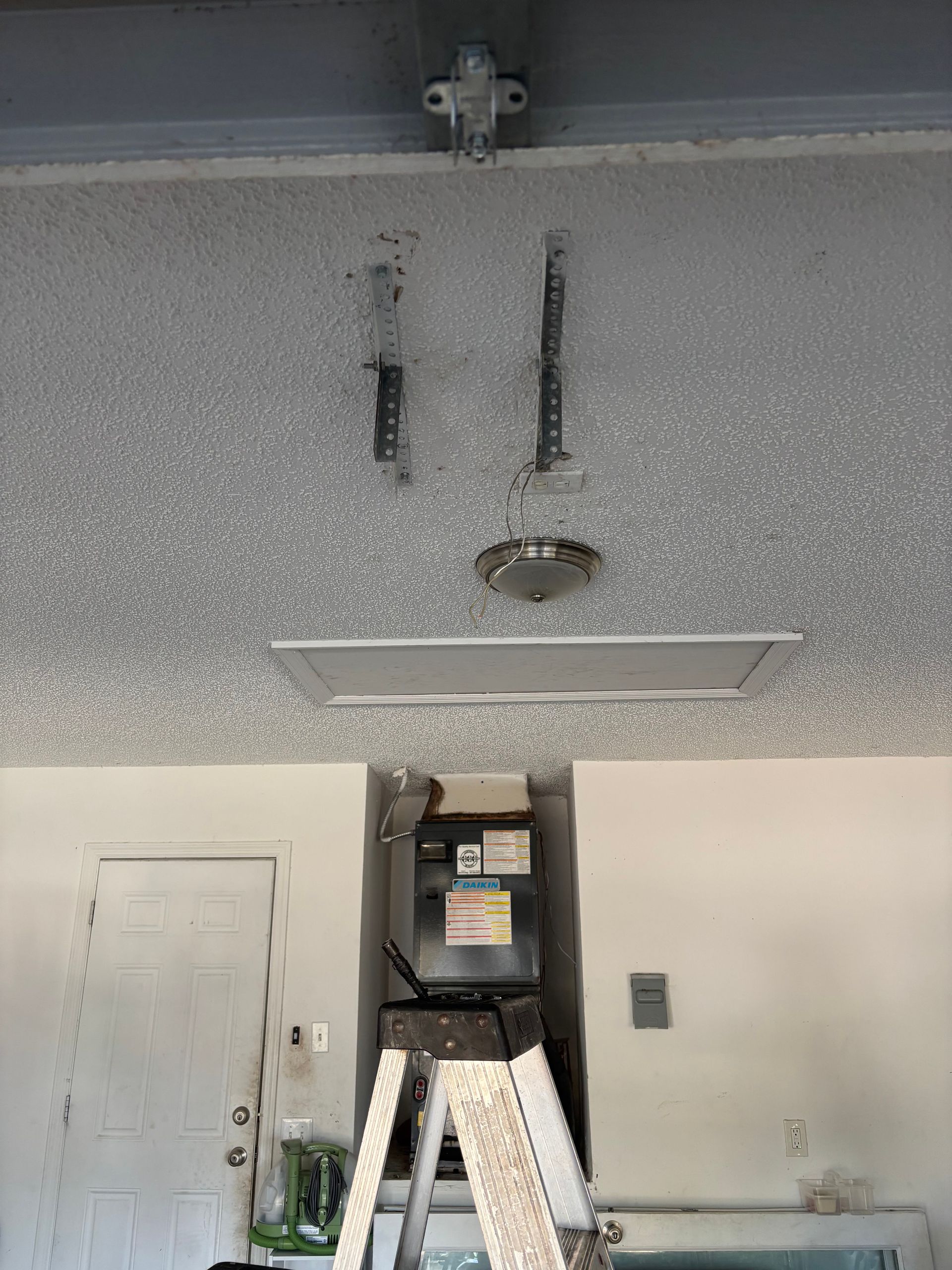 Garage interior with a stepladder under an open ceiling panel and visible hanging wires.