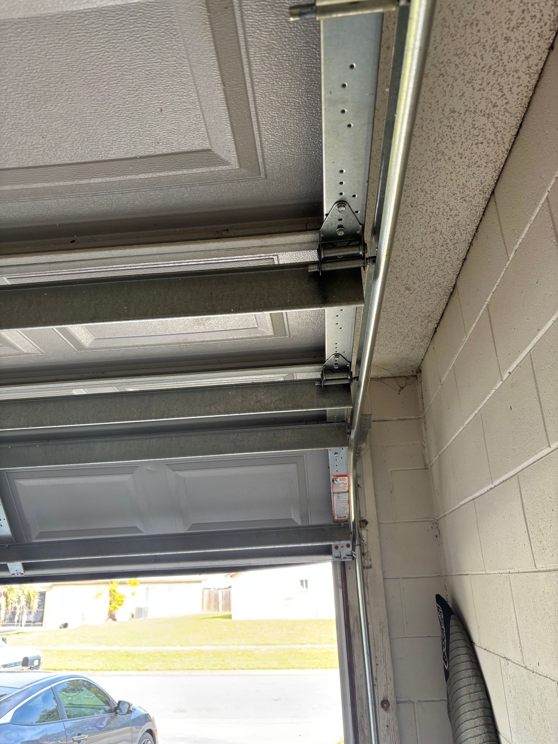 Underside of a metal garage door track and ceiling in a parking area, with a car visible outside.