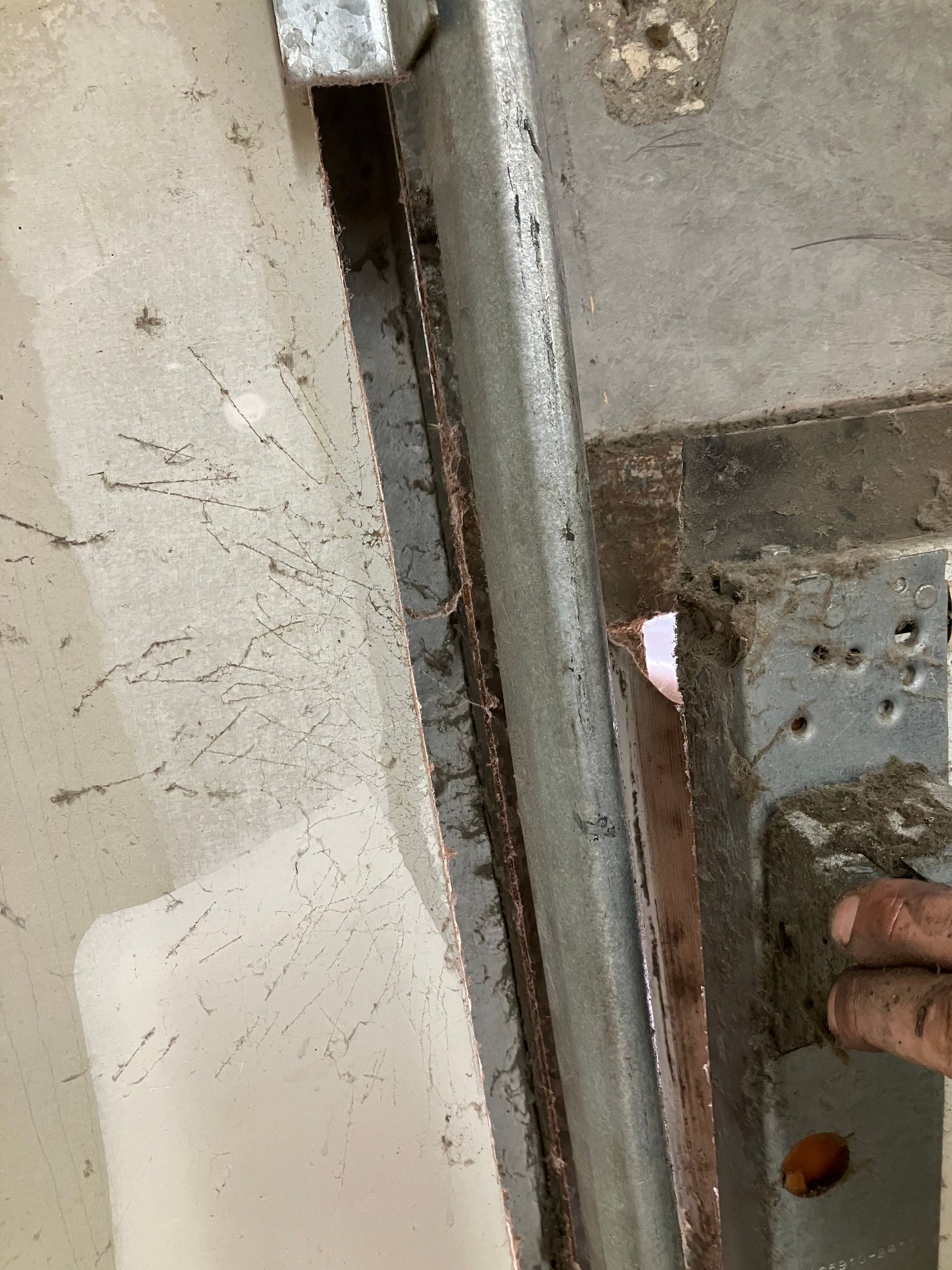 Close-up of a metal door latch being held by a hand against a worn wall.